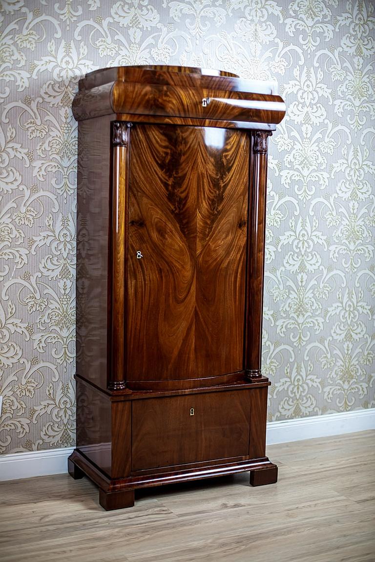 We present you this piece of furniture in the form of a post.
Made of mahogany wood and partially veneered.
It is from the first half of the 19th century.
The body is composed of a deep drawer at the bottom, a single-leaf cabinet flanked by small