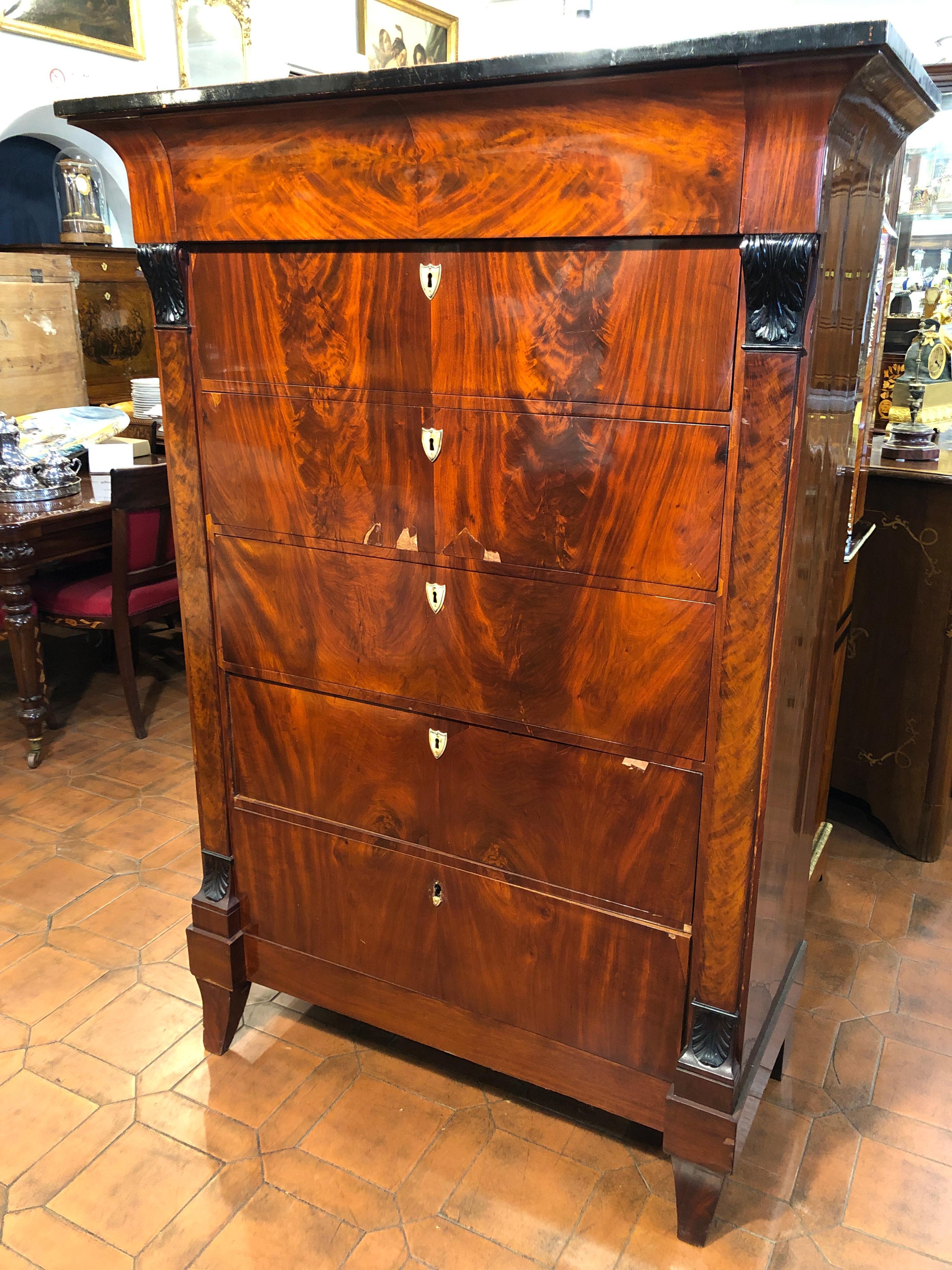 Imposing German tallboy, linear shapes, embellished with capitals, on columns, ebonized. In full Biedermeier style both as lines and as epoch, it has the upper part flared and moved, also with the ebonized edge. Beautiful quality figured mahogany.