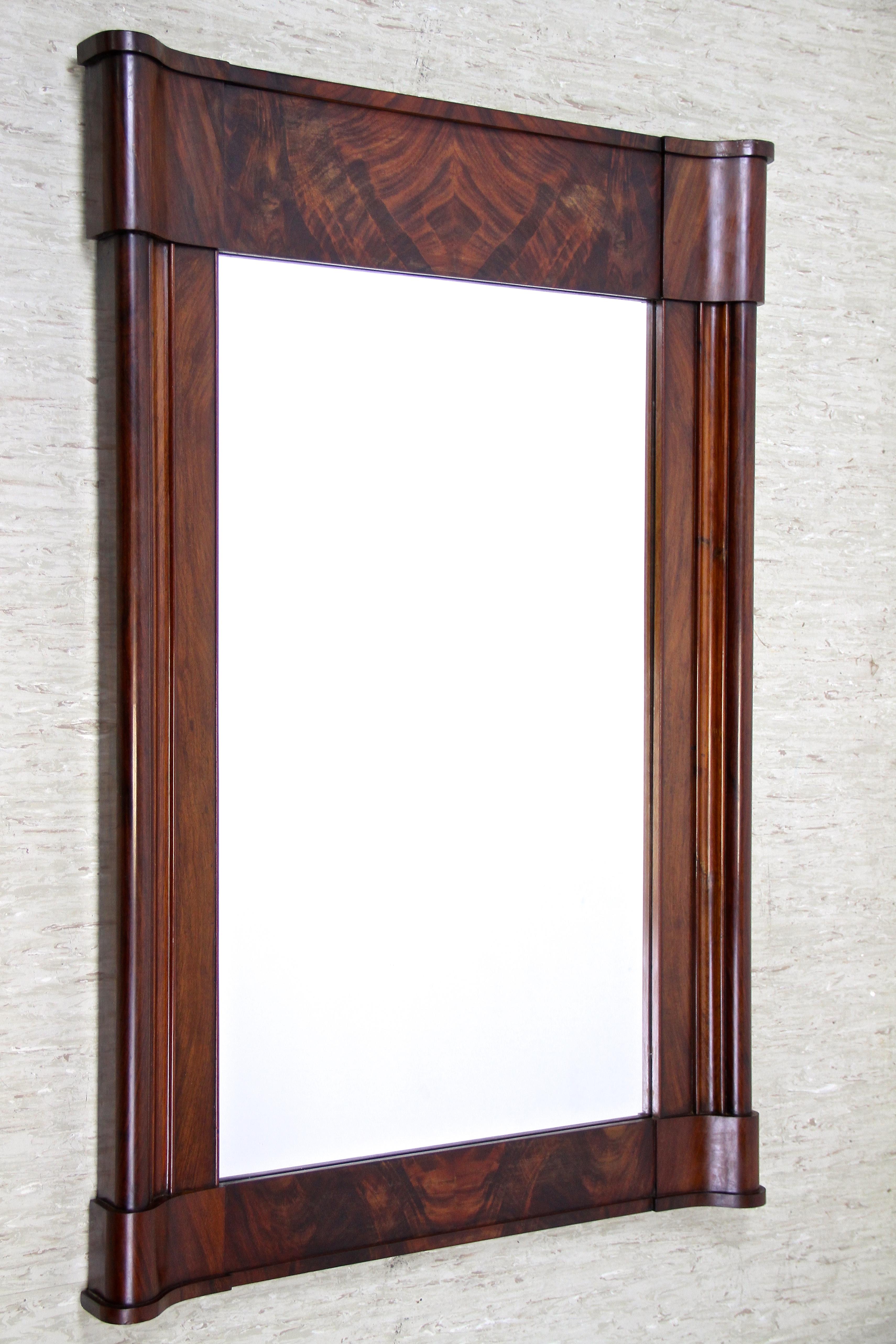 Extraordinary 19th century Biedermeier mahogany wall mirror from the famous period around 1840 in Austria. The large, unusual shaped frame impresses with its artfully design and shows a beautiful book matched pyramid mahogany veneered surface. The