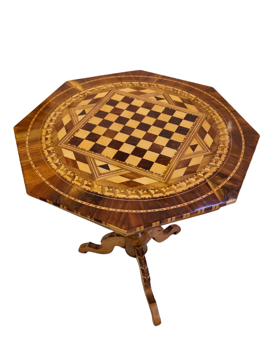 An elegant Biedermeier chess table from circa 1830, featuring a finely inlaid marquetry top with a central chessboard surrounded by intricate geometric and ornamental patterns. The octagonal tabletop is veneered in various precious woods, showcasing