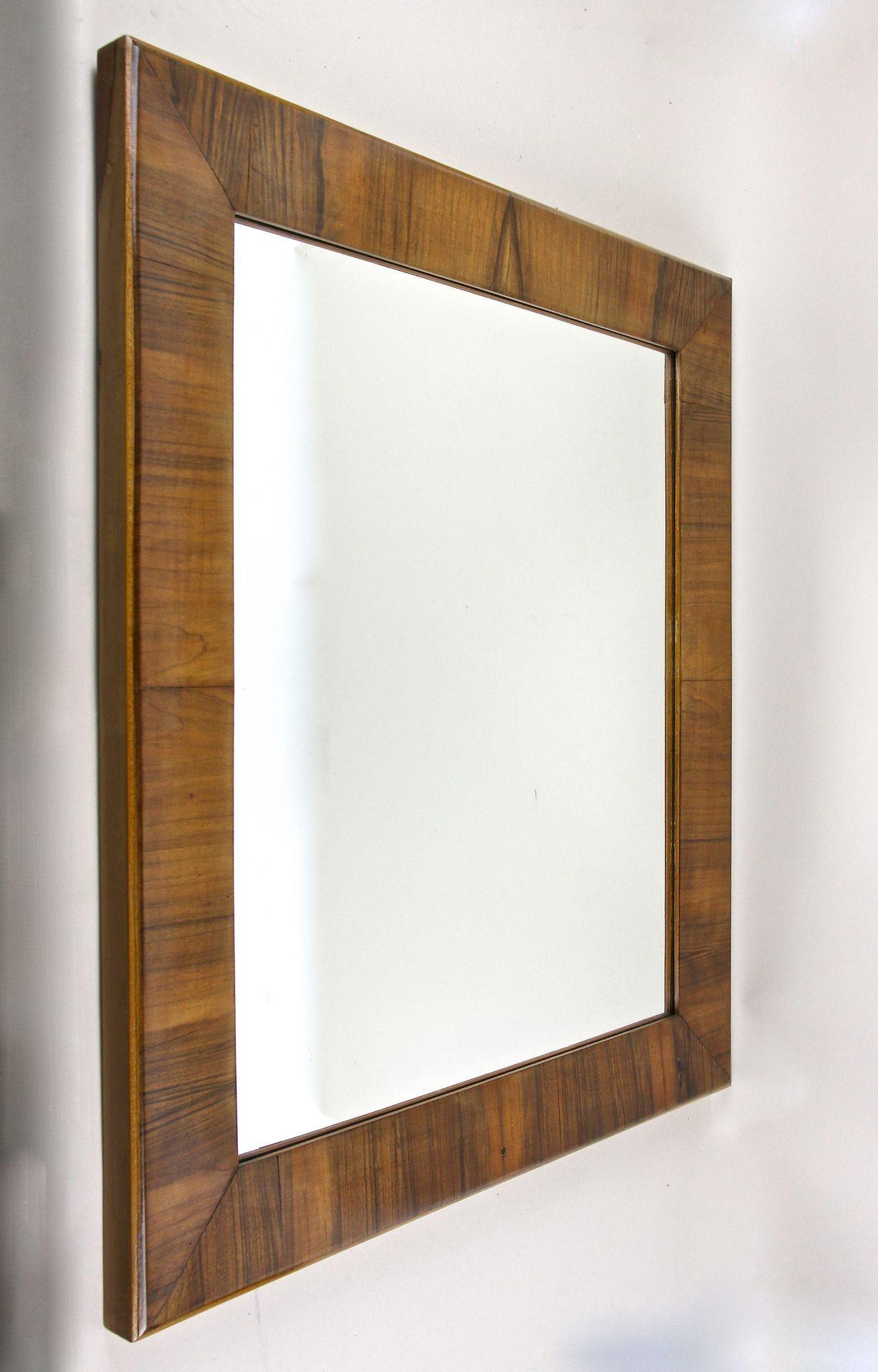Charming 19th century nutwood wall mirror from the famous Biedermeier era in Vienna/ Austria around 1840. This eyecatching antique Biedermeier wall mirror comes with a traditional substructure made of spruce wood and impresses with its beautiful,