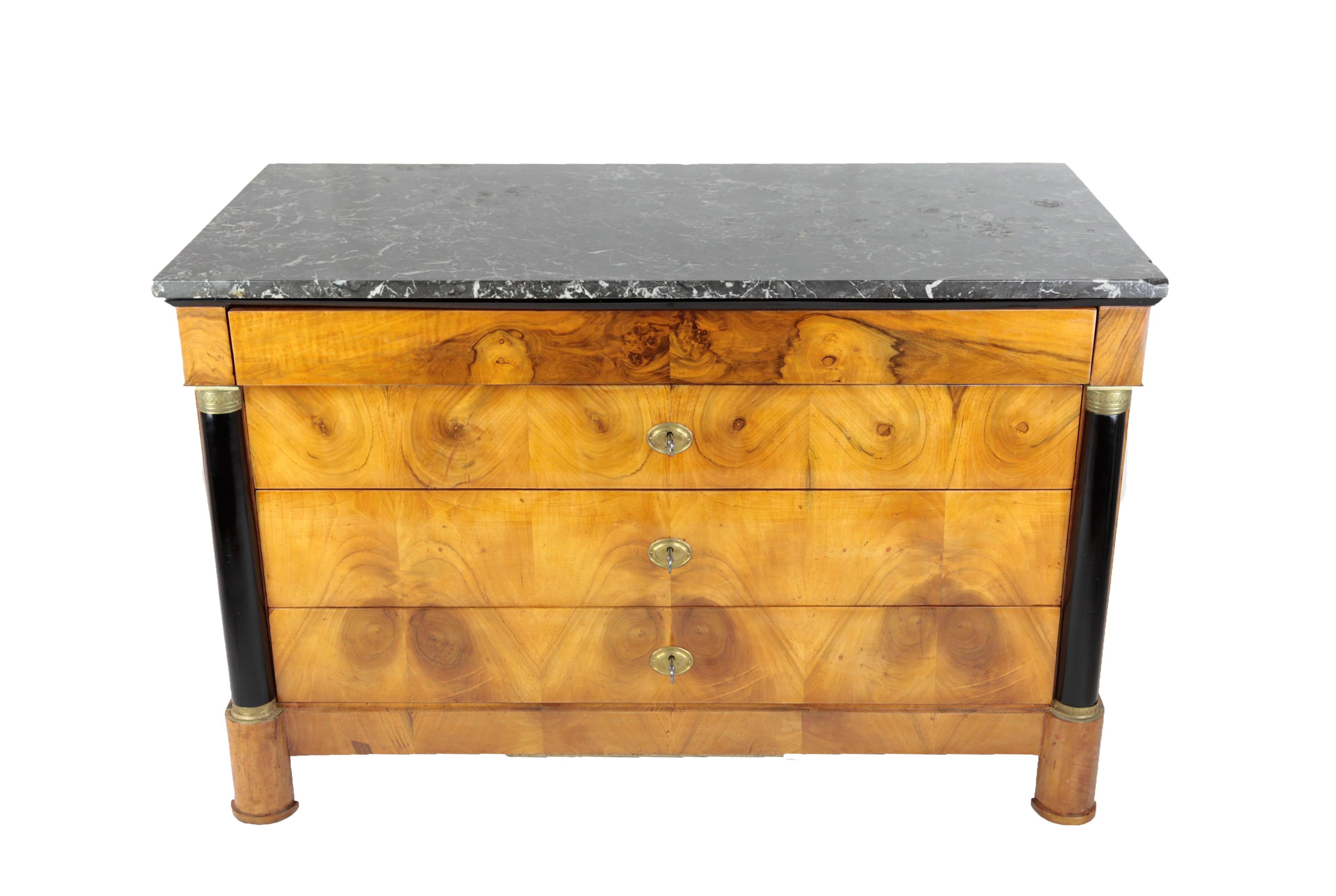 The Biedermeier chest of drawers with 4 drawers, designed in a straight line with ebonized columns with brass mountings, was created circa 1820 in France. The drawers differ in size, the top drawer is slightly smaller and created as a hidden drawer,