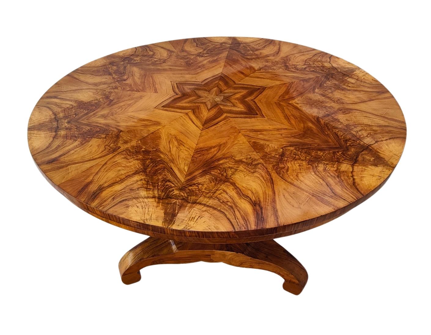 This elegant 19th-century Biedermeier round salon table showcases the timeless beauty of walnut veneer in a stunning starburst marquetry design. Crafted in Germany circa 1825, the tabletop features bookmatched walnut grain arranged in a symmetrical,