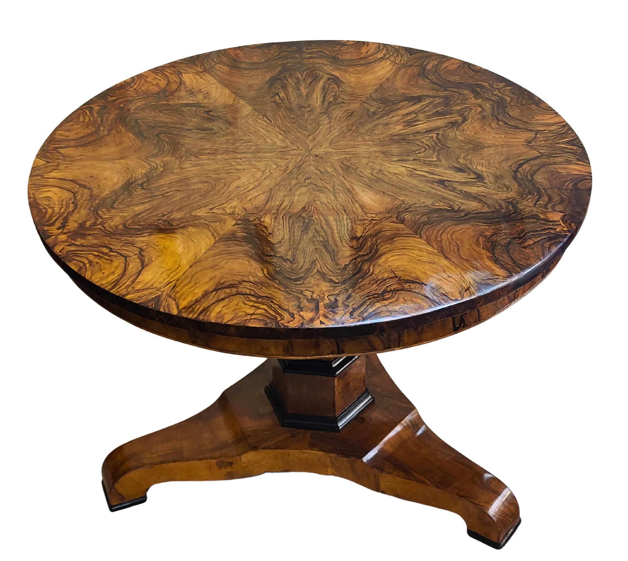 Raffinato tavolo da salotto rotondo Biedermeier in noce dell'inizio del XIX secolo. Il piano circolare è impiallacciato in radica di noce riccamente figurata e disposta a raggiera che si legge magnificamente da ogni angolazione. Lo spesso grembiule