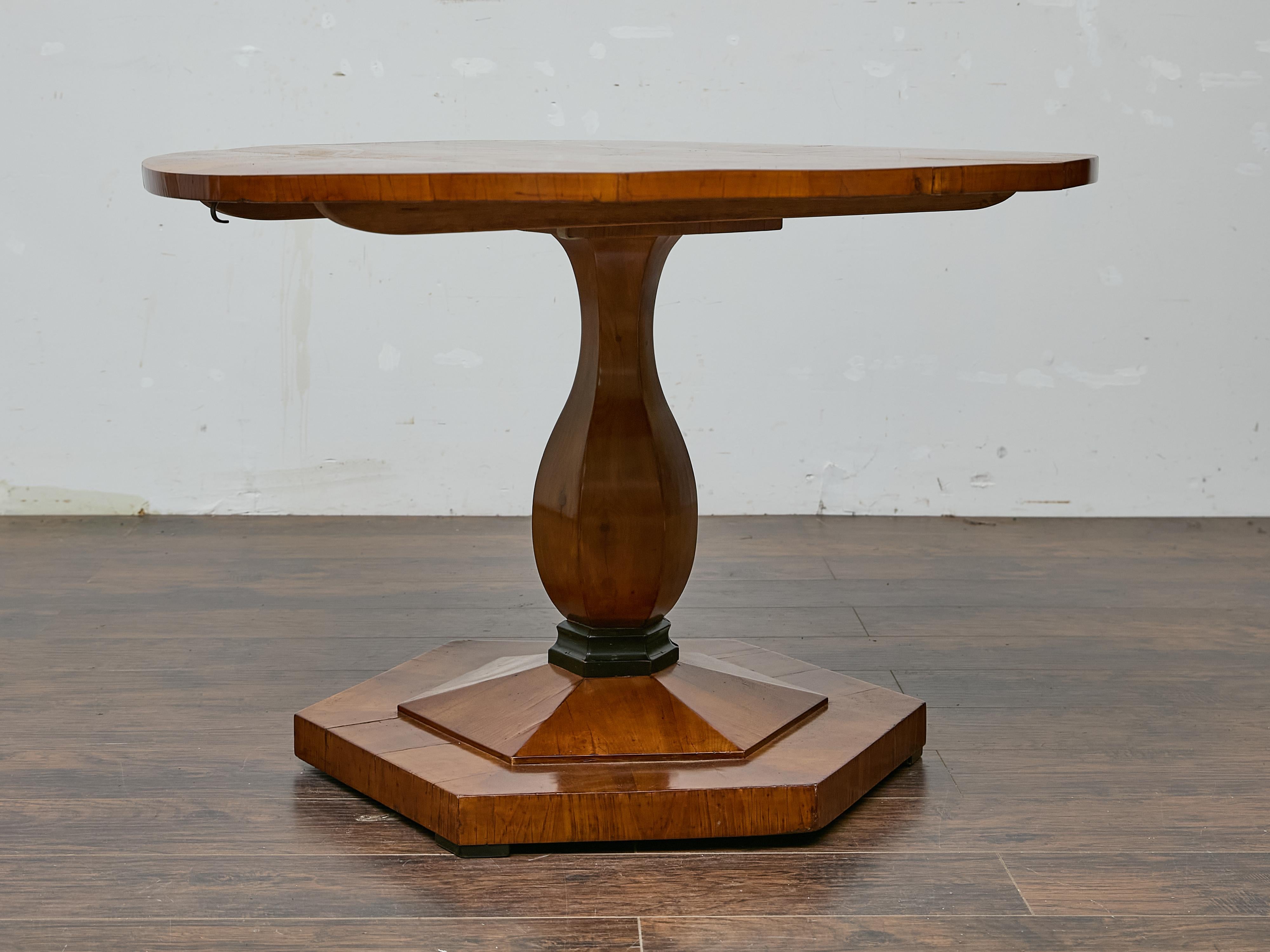 This early 19th-century Austrian Biedermeier center table presents an elegant balance of architectural restraint and rich natural material. Crafted from warmly toned walnut, the circular top features a striking sunburst veneer pattern, with the