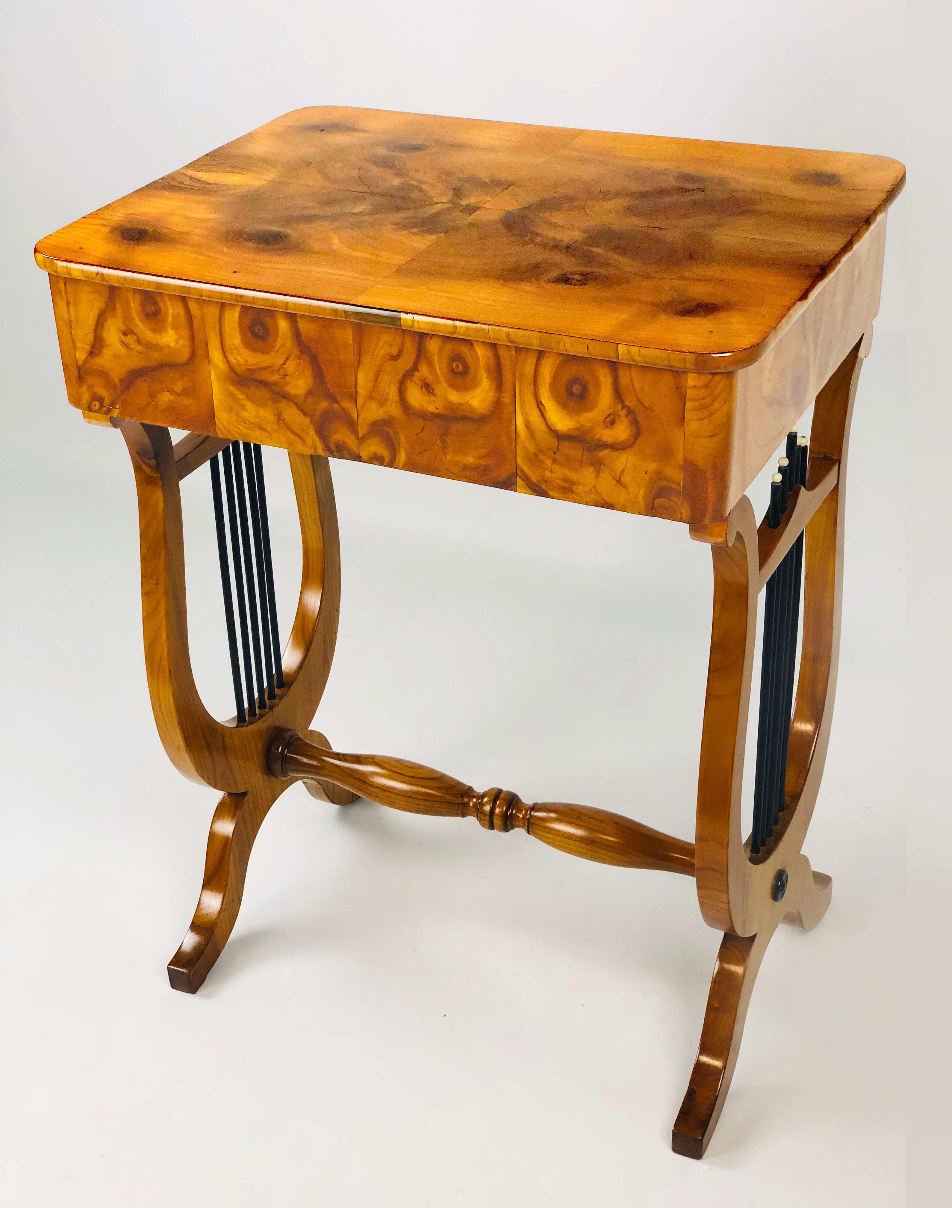 Outstanding early 19th century German Biedermeier sewing side table with twin lyre base, the top and aprons adorned with rare oyster walnut veneer. The single drawer has several small compartments and an original folding needle cushion. The top is