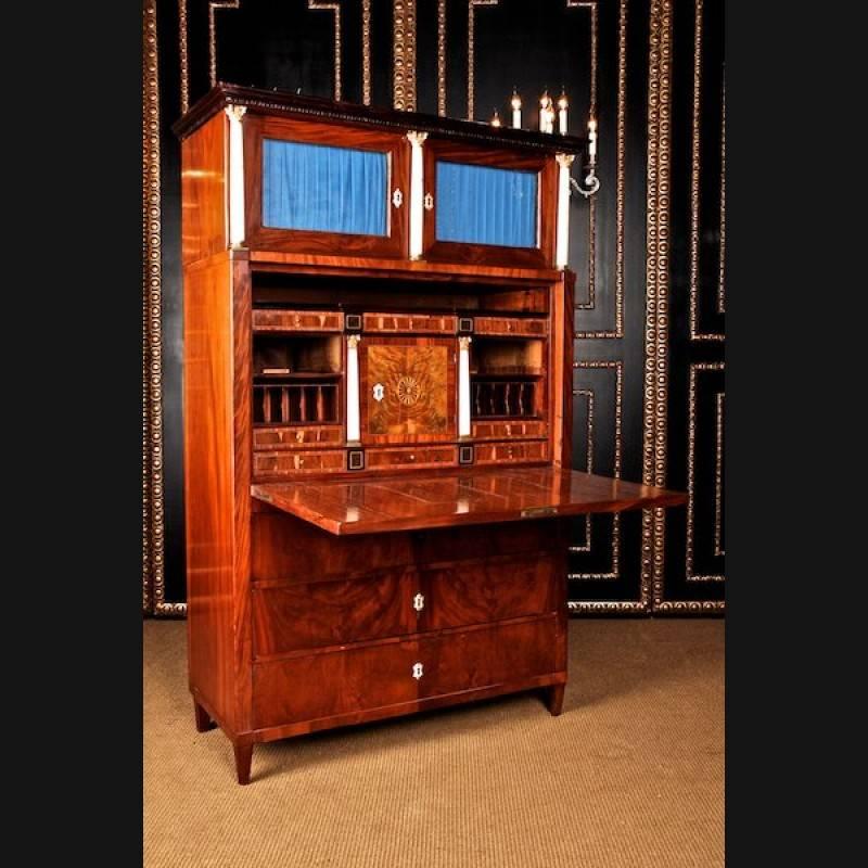 Classicist secretary, circa 1800-1810.
Cuba mahogany on solid softwood partly ebonized. High-right, architecturally designed body on conical legs. In the front three drawers. Straight writing board, behind it architectural interior life with secret