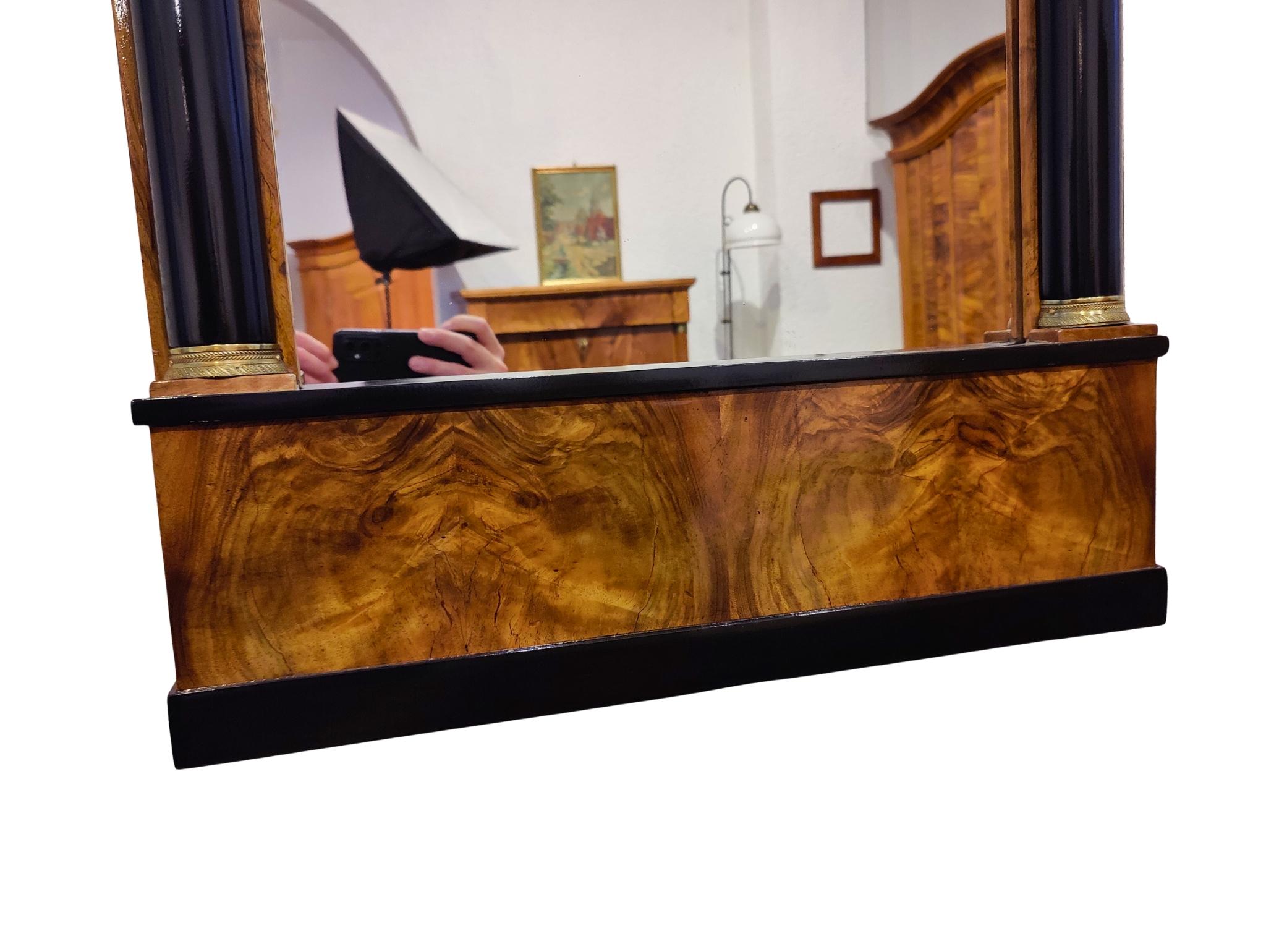 Cet élégant miroir mural Biedermeier a été fabriqué en Allemagne vers 1820 et représente le style raffiné du début du XIXe siècle. Le cadre est plaqué en noyer magnifiquement figuré, présentant une couleur chaude et un motif de grain saisissant. Sa