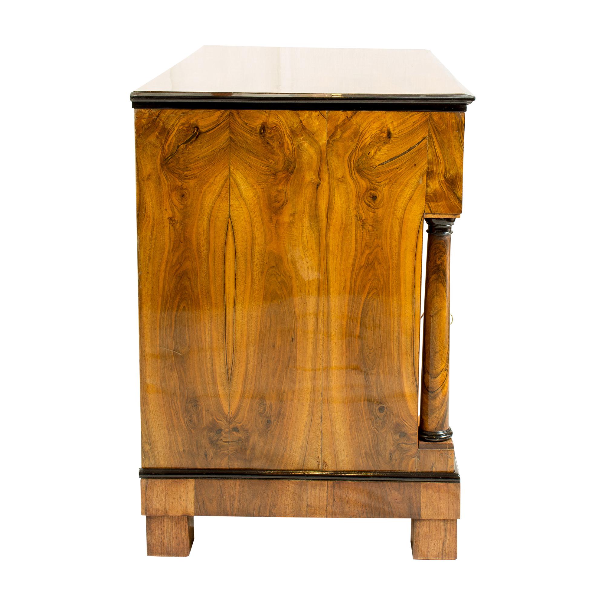 The chest of drawers dates from the Biedermeier period. The chest of drawers has a beautiful walnut veneer picture, which covers a spruce wood body. The front is convex shaped and is flanked by two solid walnut columns. Fine shellac polish.