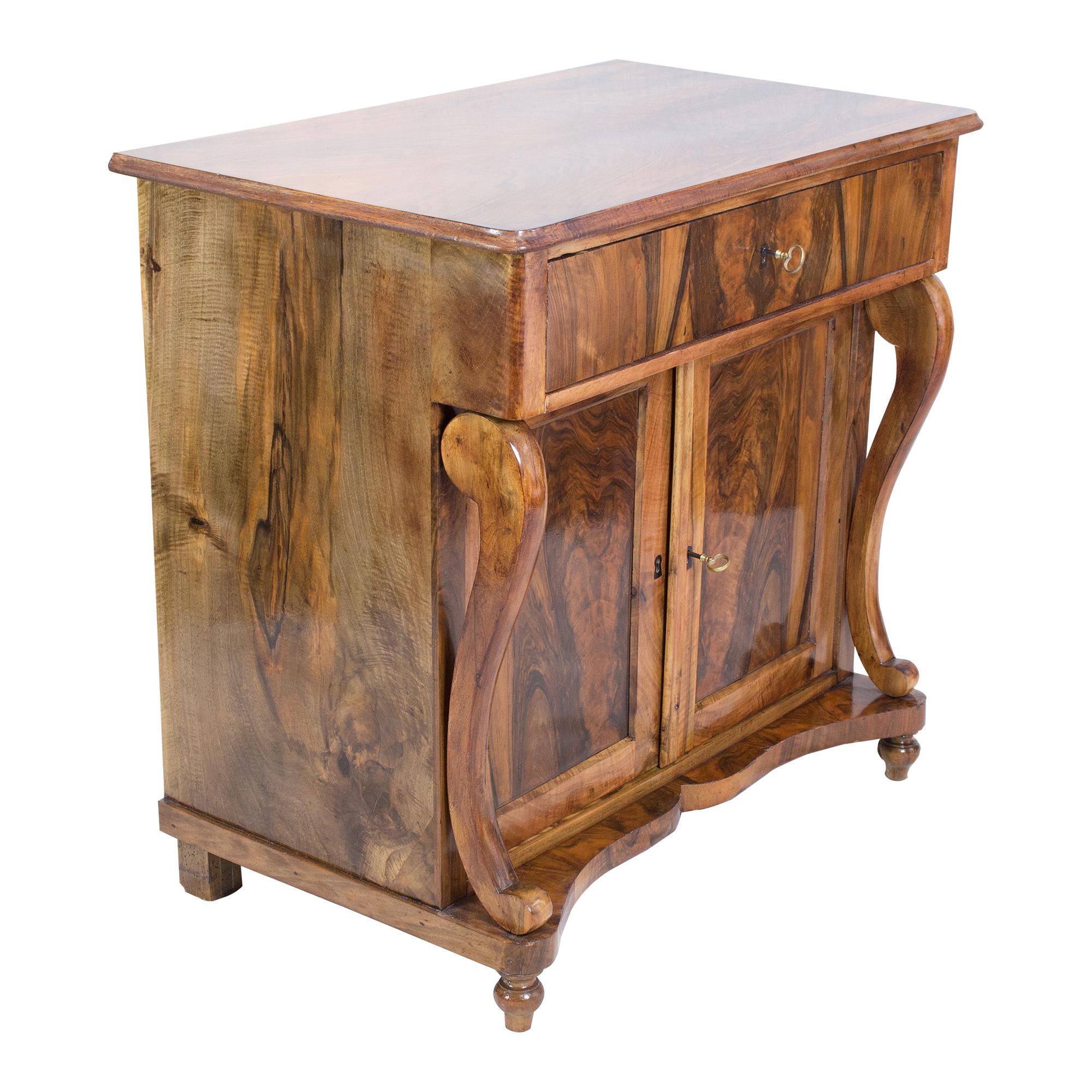 Dieses schöne Möbelstück ist ein Konsolen-Halbschrank aus dem Biedermeier. Der Halbschrank ist aus furniertem Nussbaumholz auf einem Fichtenkorpus und teilweise auch aus massivem Nussbaumholz gefertigt. Unter dem Deckel befindet sich eine Schublade