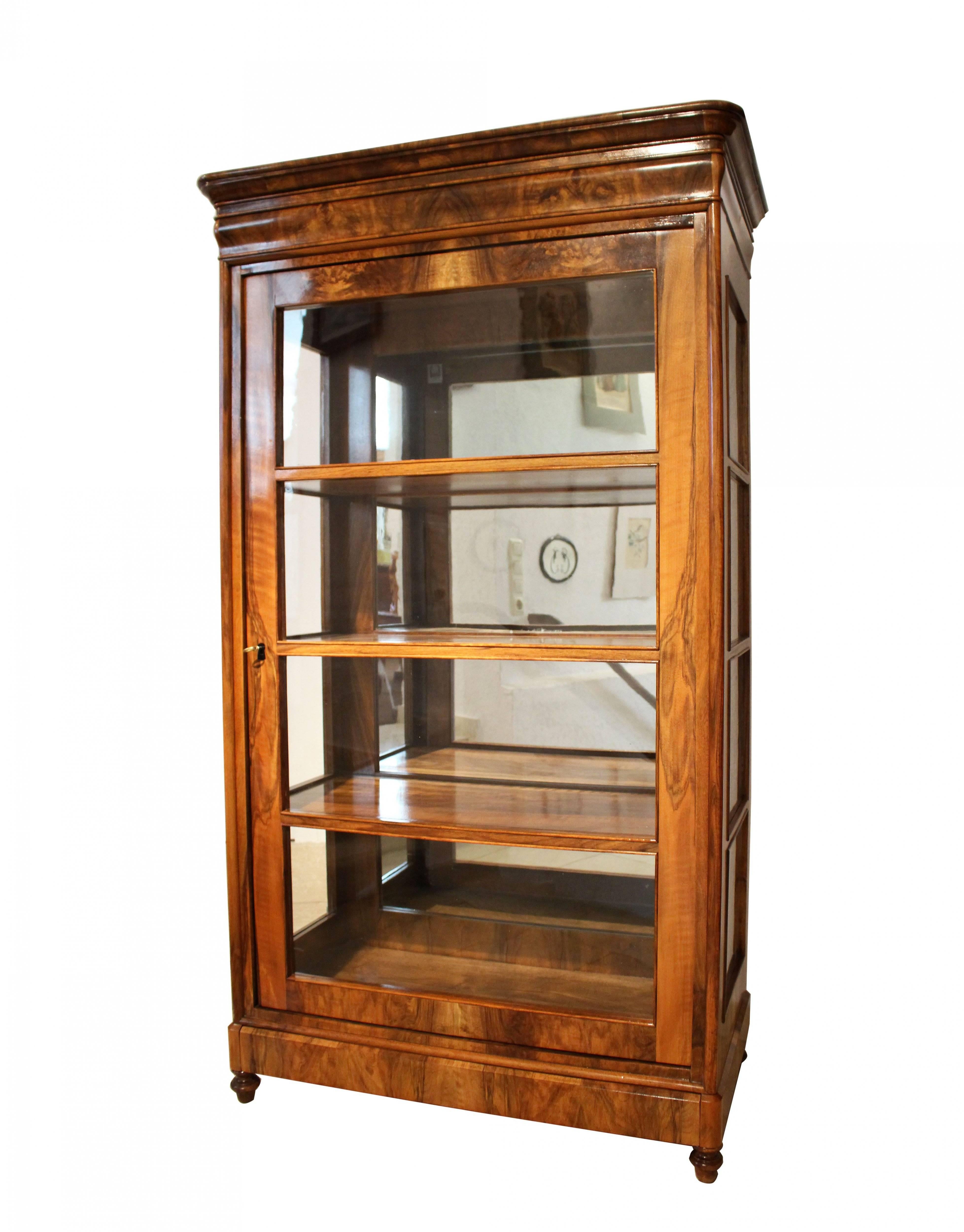 Very nice three-sided showcase with a continuous veneer picture. The top is also veneered. The display case dates from the time of the Biedermeier period, circa 1820. The shelves are made of solid walnut. The base contains a drawer or secret