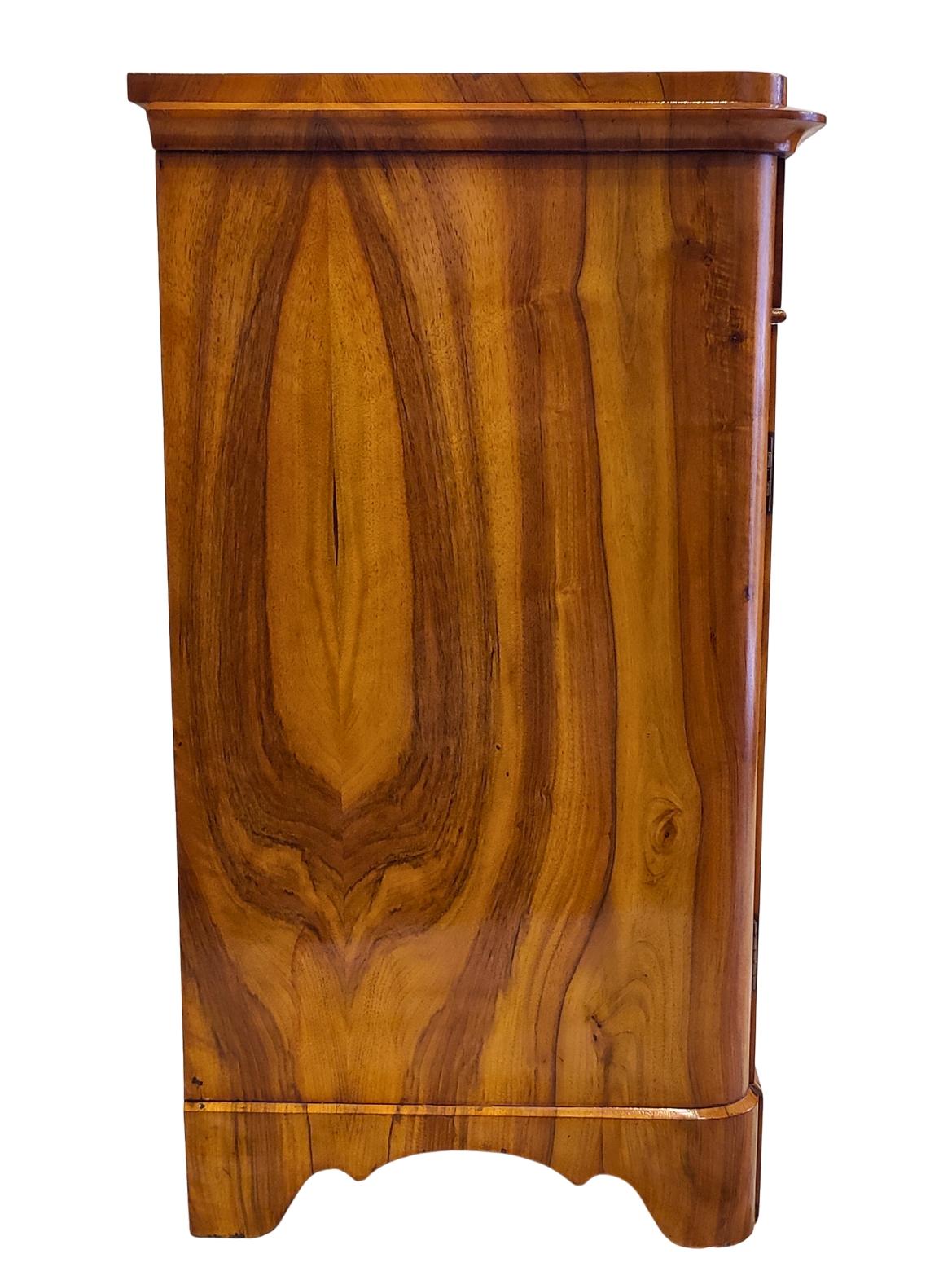 Dieser elegante Biedermeier-Halbschrank wurde um 1830 in Süddeutschland gefertigt. Das Möbelstück ist mit schön gemasertem Nussbaum furniert und weist ein auffälliges, an die Bücher angepasstes Muster auf. Das Innere ist aus Weichholz und Eiche