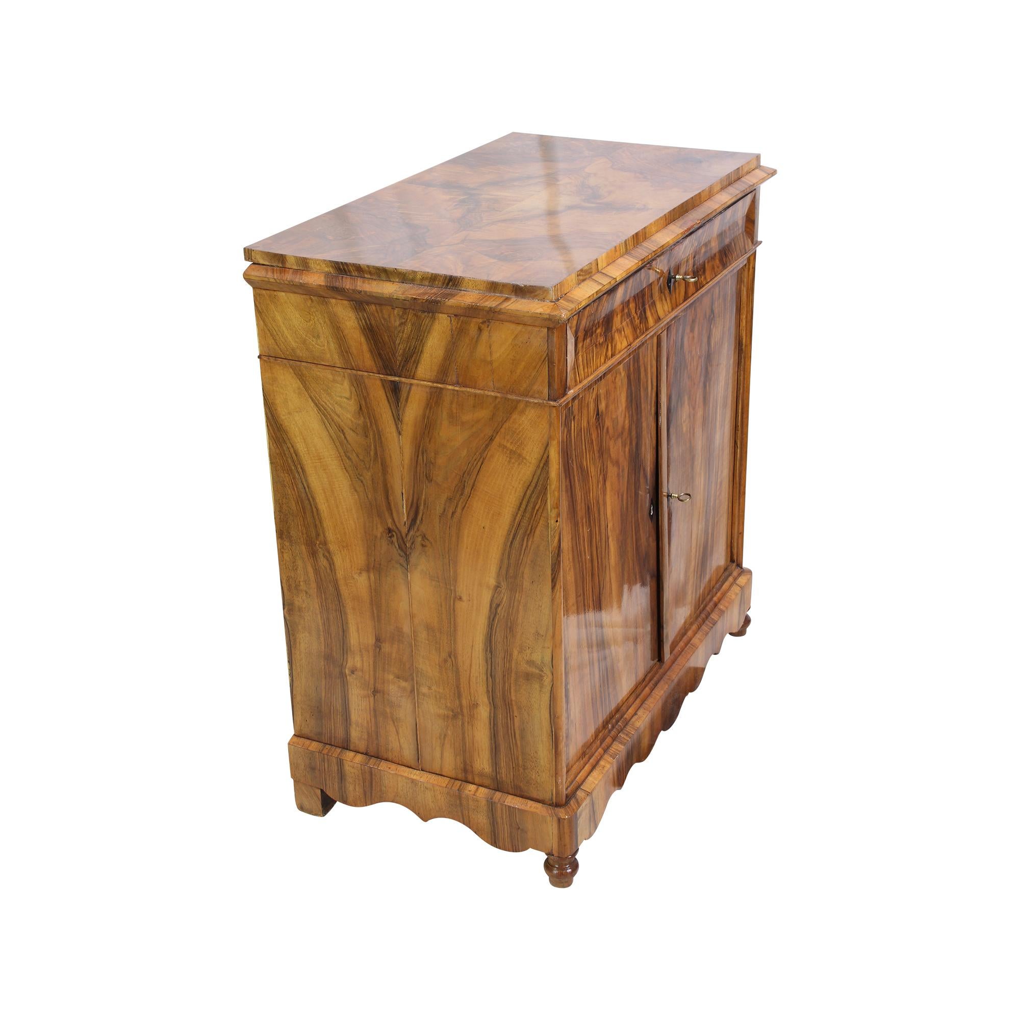 Schöner Biedermeier Halbschrank aus der Biedermeierzeit um 1830. Die Möbel sind mit schönem Nussbaumfurnier mit einem schönen durchgehenden Furniermuster auf einem Fichtenkorpus überzogen.
Oben gibt es eine Schublade und unten zwei Türen. Der Körper