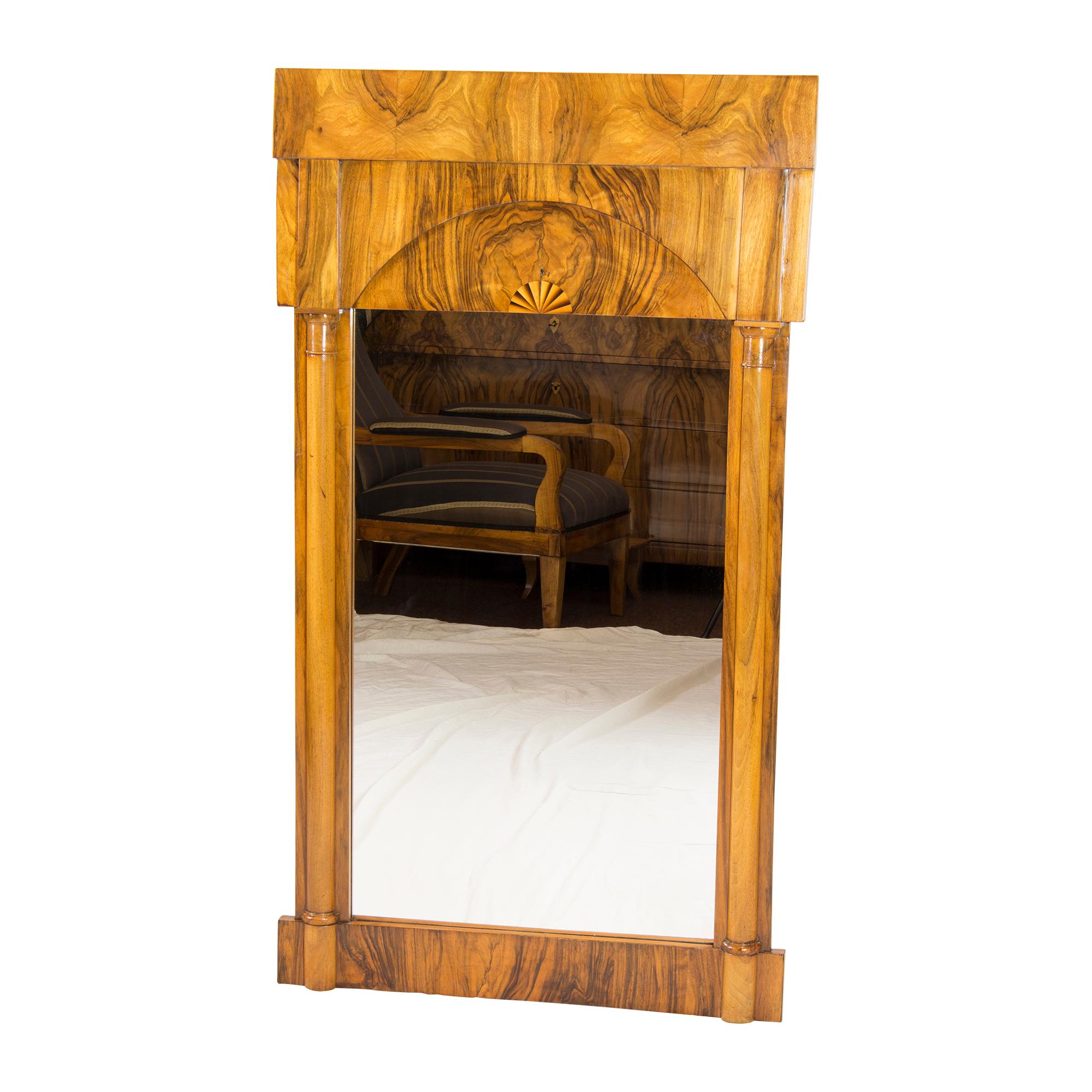 Biedermeier column mirror dates from around 1820 and was made of walnut. The upper part is curved to the back and has a beautiful inlay work in the wood. The mirror glass was renewed. 
Very good hand polished restored condition.