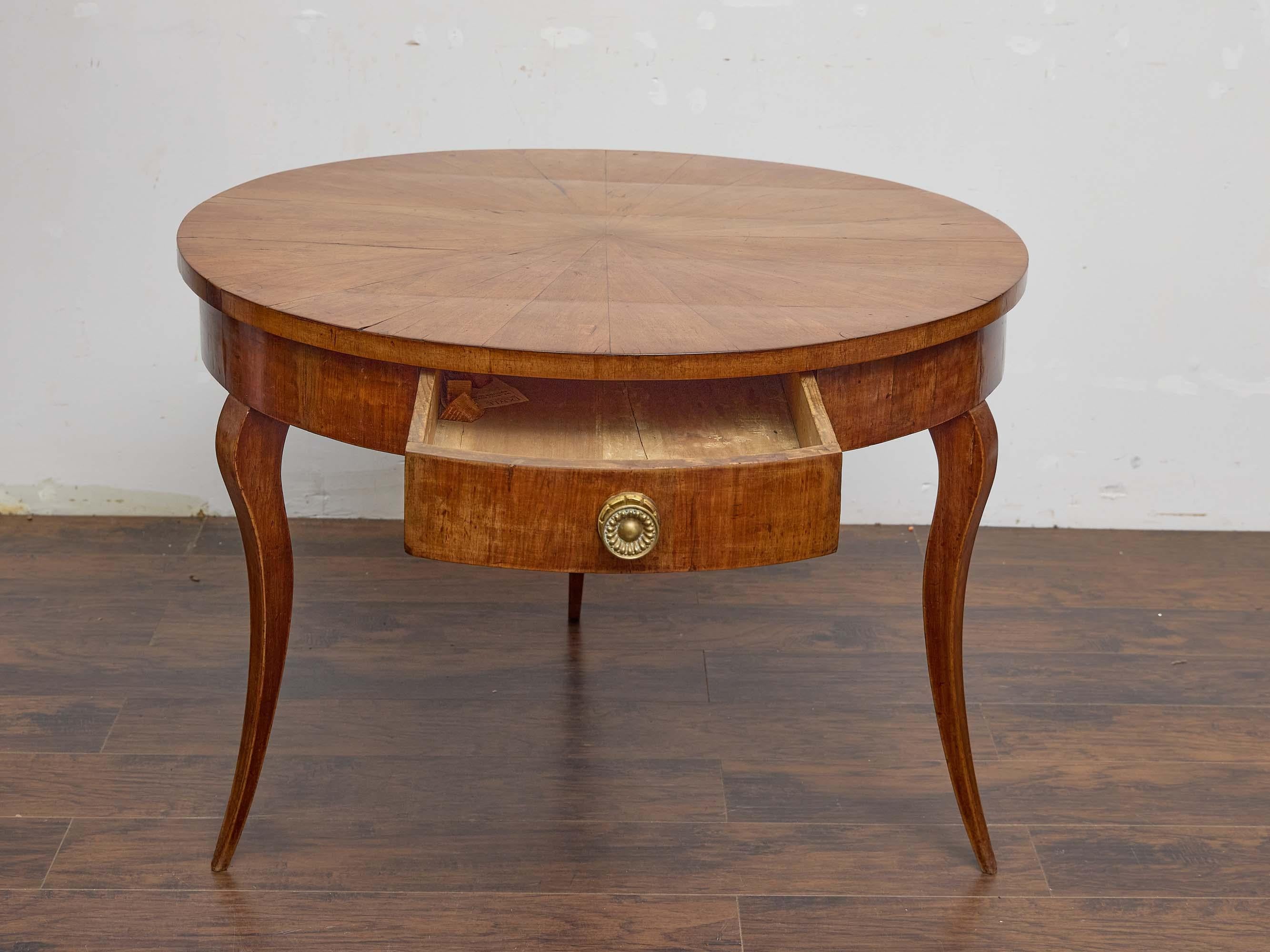 A 19th-century Biedermeier walnut round center table, showcasing the elegance and balance characteristic of the period. The circular top is veneered in walnut, arranged in a striking radiating sunburst pattern that highlights the natural grain and