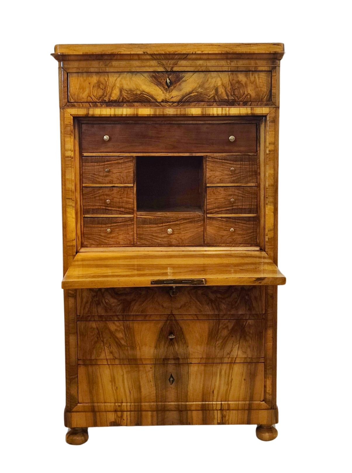 Questa splendida scrivania Biedermeier è un autentico pezzo d'antiquariato realizzato in legno di noce, sia all'interno che all'esterno. Risalente agli inizi del XIX secolo, questo capolavoro mostra la classica eleganza e la semplicità tipiche del