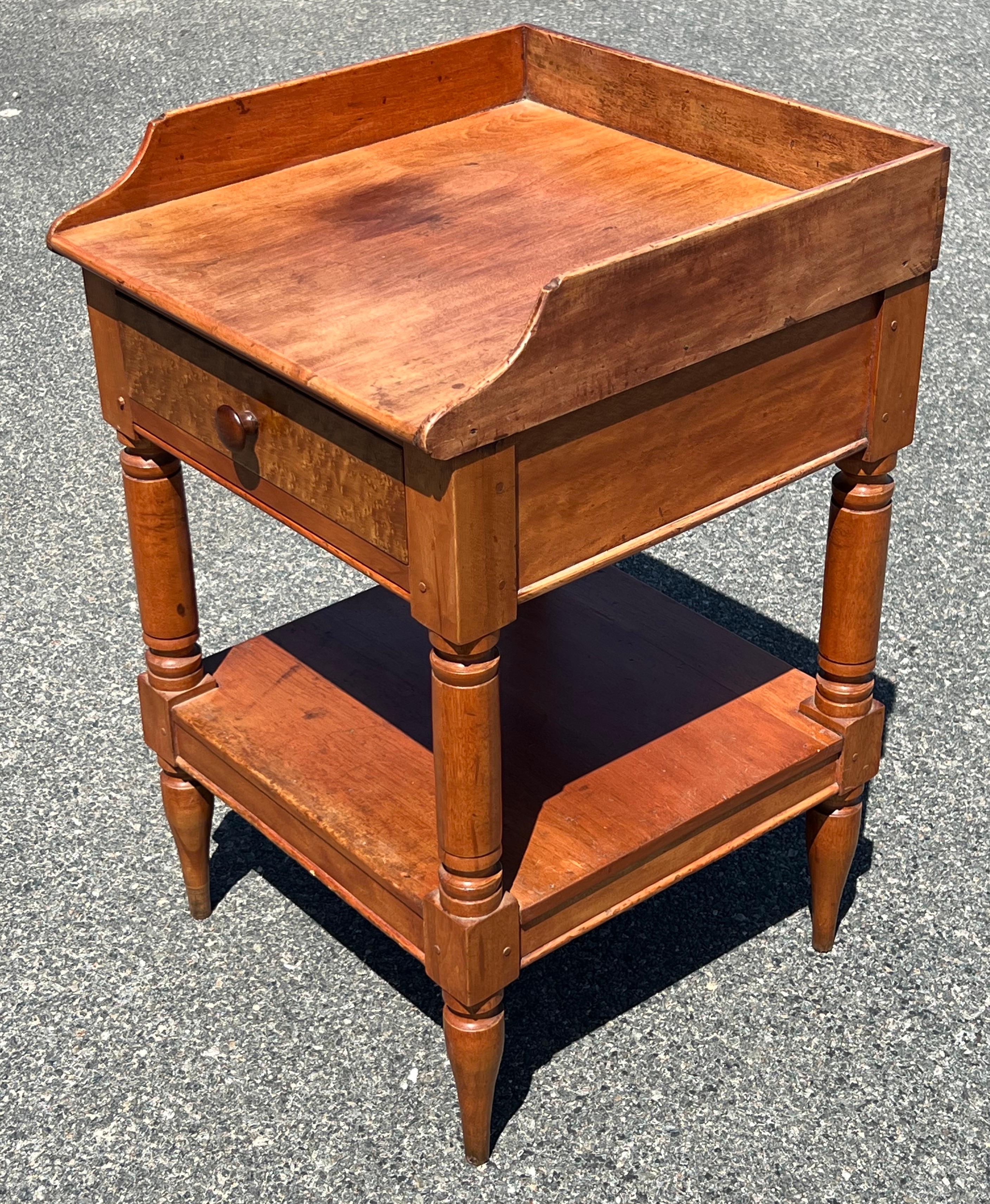 19th century two tier stand in birch. Upper gallery with shaped sides, single drawer with figured Birdseye Maple drawer front and turned wooden knob. With lower shelf and turned legs. Surface height 28.25 inches.