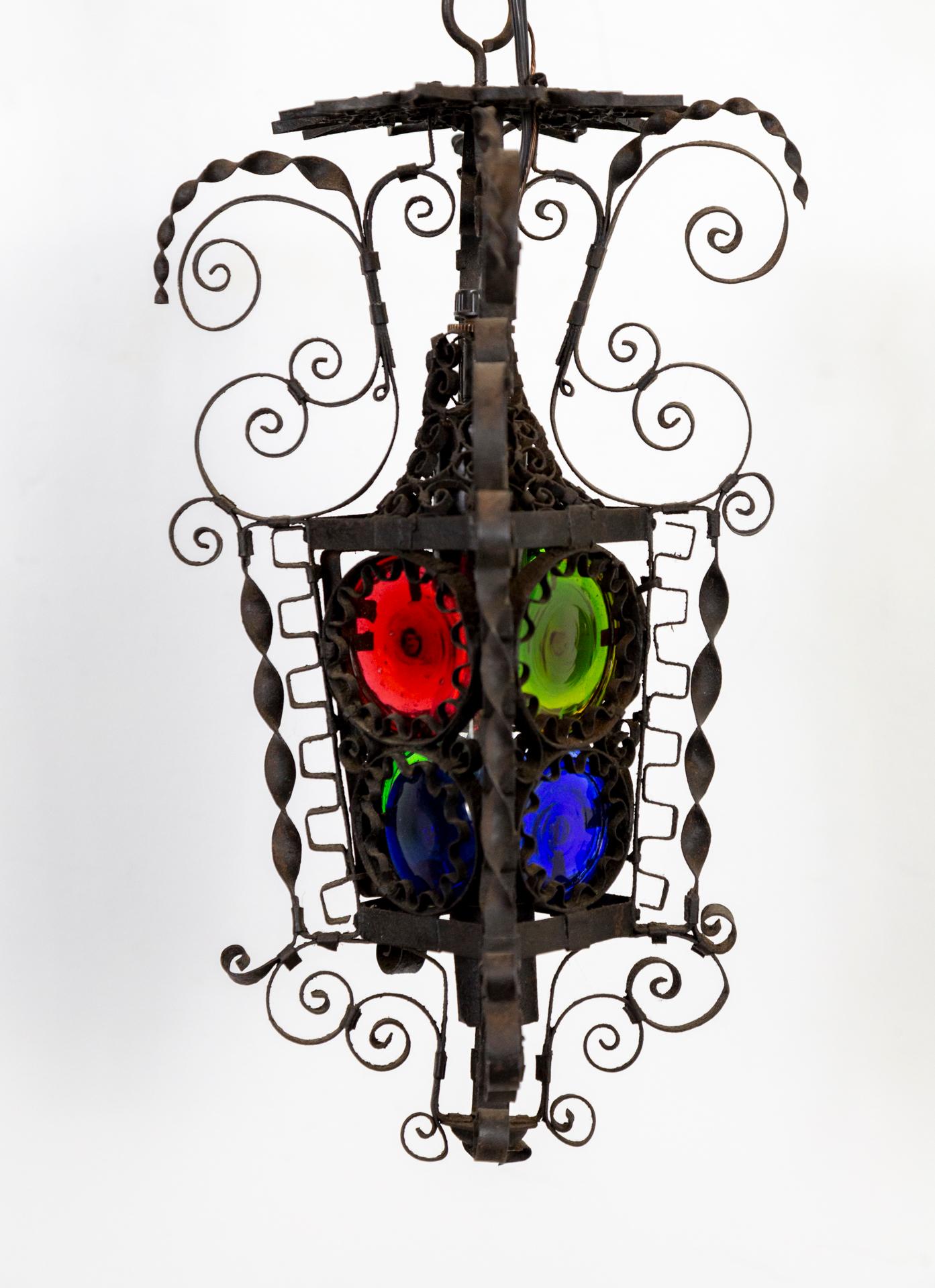 A lavishly decorated, 19th century, Italian, wall hanging lantern composed of complex, twisted and curled blackened iron. With a long, multi-dimensional filigree chain; and ornamented structure holding primary colored, handmade, glass disks. Newly