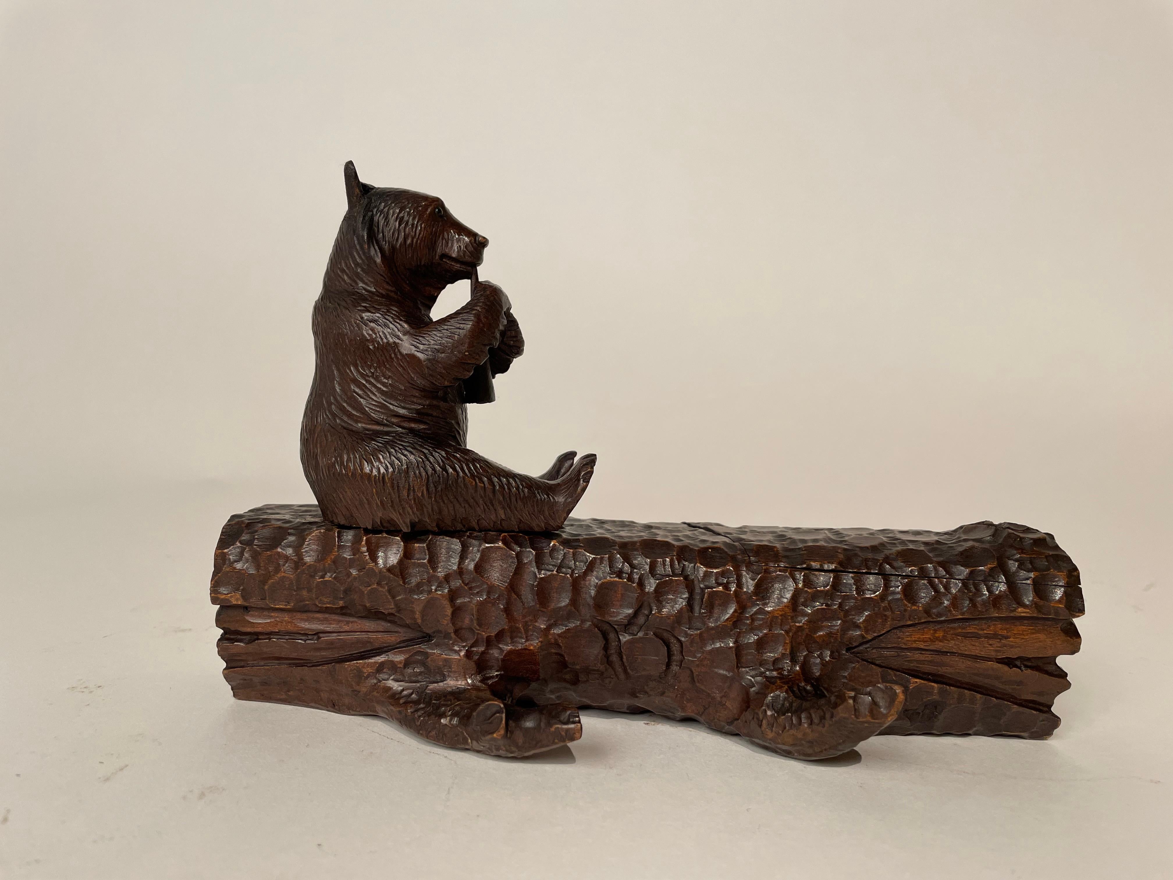 Charming black forest carving of a bear playing the flute seated om a log. The log opens on one end to reveal a glass inkwell, and the bear swivels to an opening to store pen nibs. Beautifully conceived design by a master carver. A fine example of
