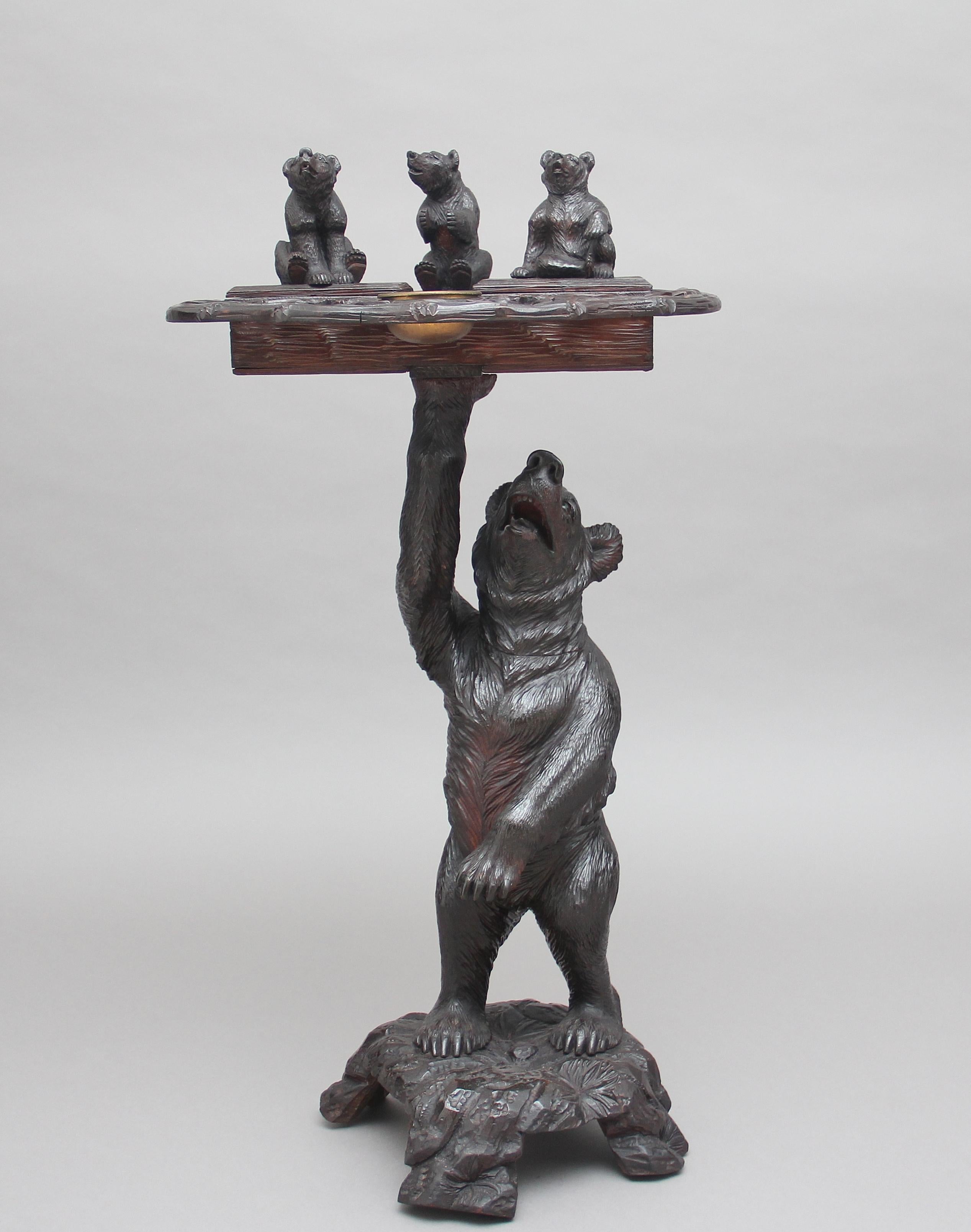 19th century black forest carved bear smokers stand, a fabulous quality item of a bear standing on a base with his arm supporting a stylized tray with three small bears, with two each sitting on a lid which opens to reveal a compartment, the main