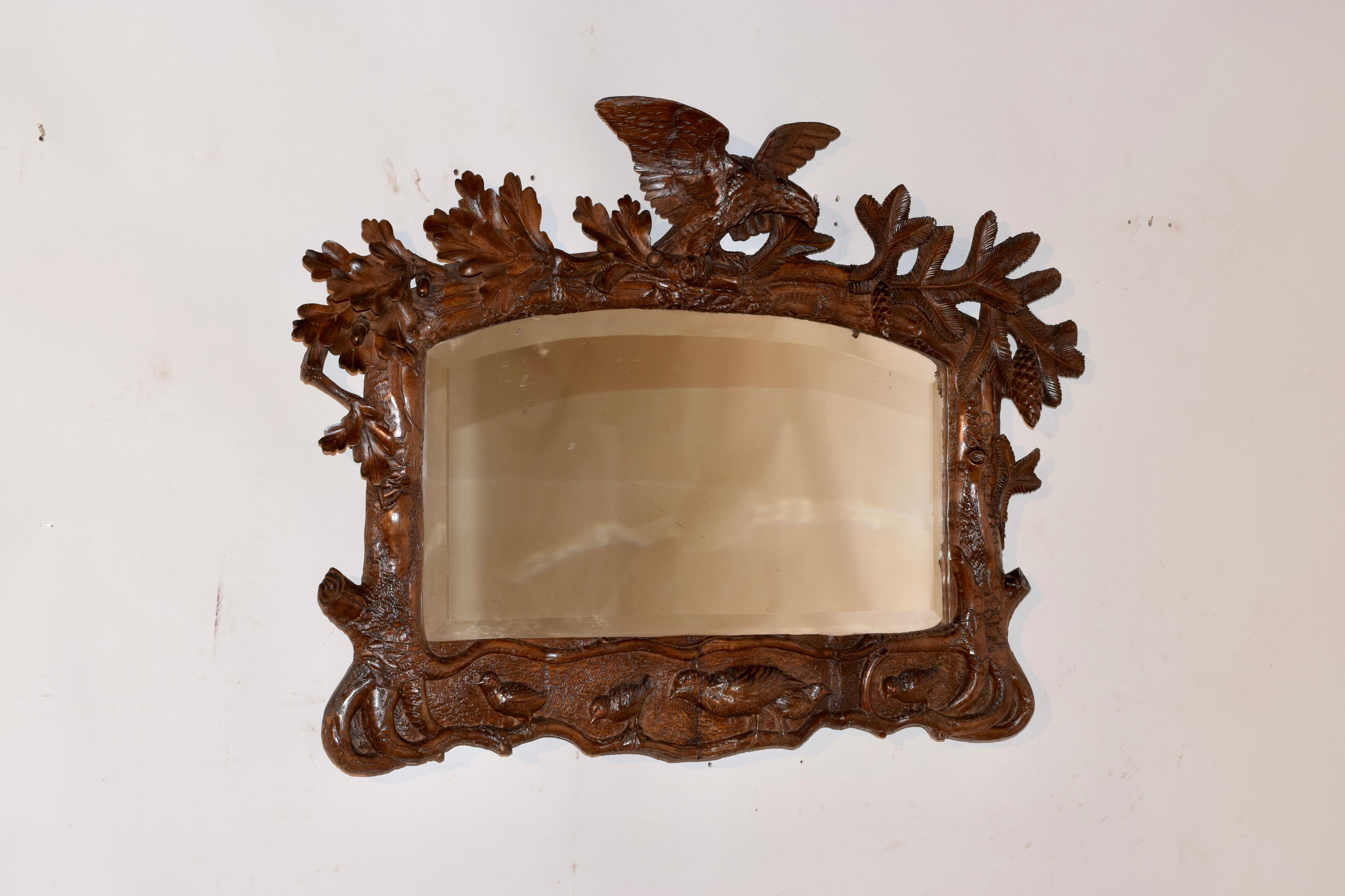 Exquisite 19th century Black Forest hand carved mirror, depicting a bird on top of detailed branches and leaves surrounding the mirror. In the lower part of the frame, there are what appear to be the roots of the tree surrounding the frame with a
