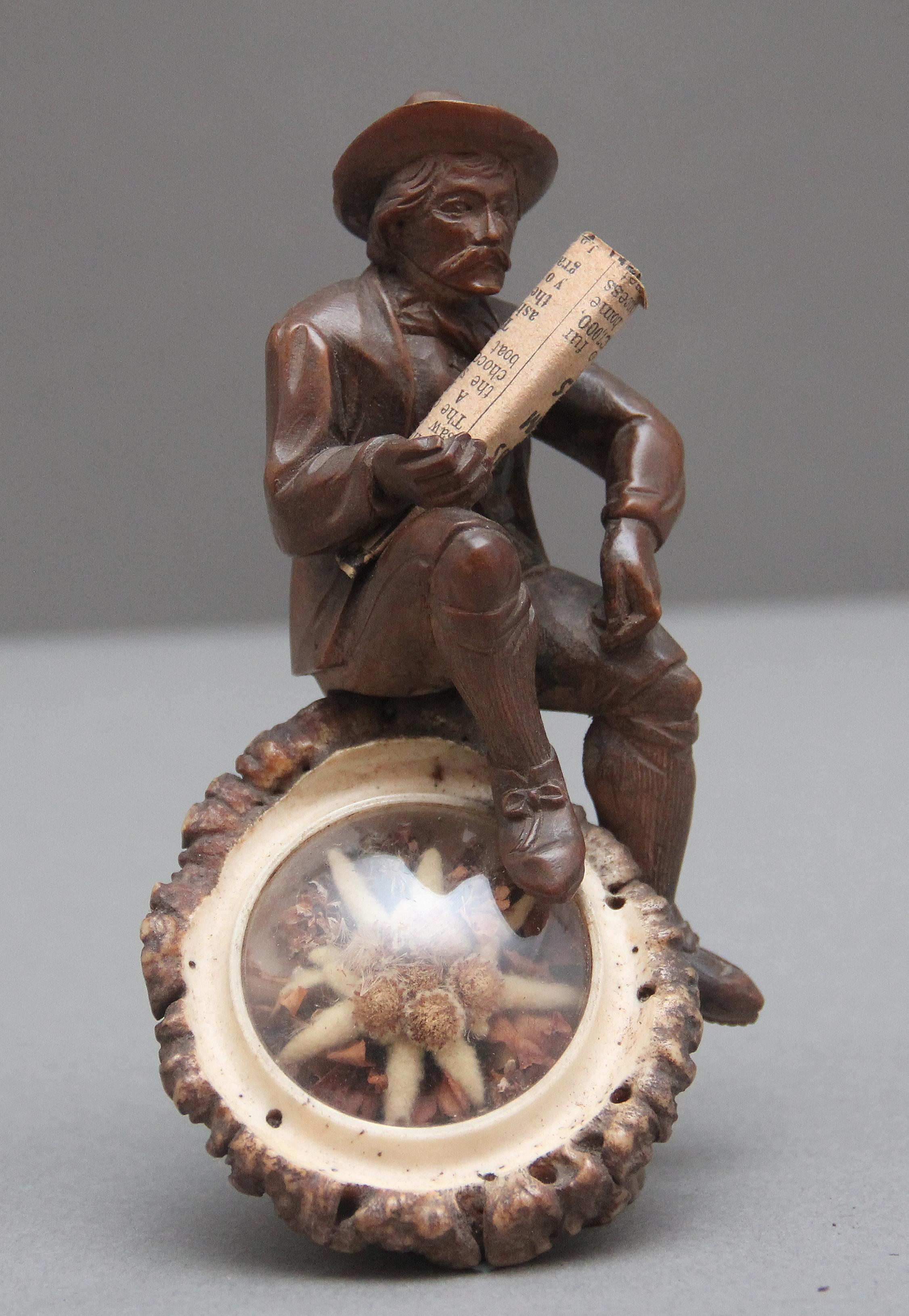 Una meravigliosa e unica scultura della Black Forest del XIX secolo raffigurante un uomo anziano seduto su un tronco d'albero con in mano un giornale; la parte anteriore del tronco d'albero, racchiusa dietro una finestra di vetro circolare, è la