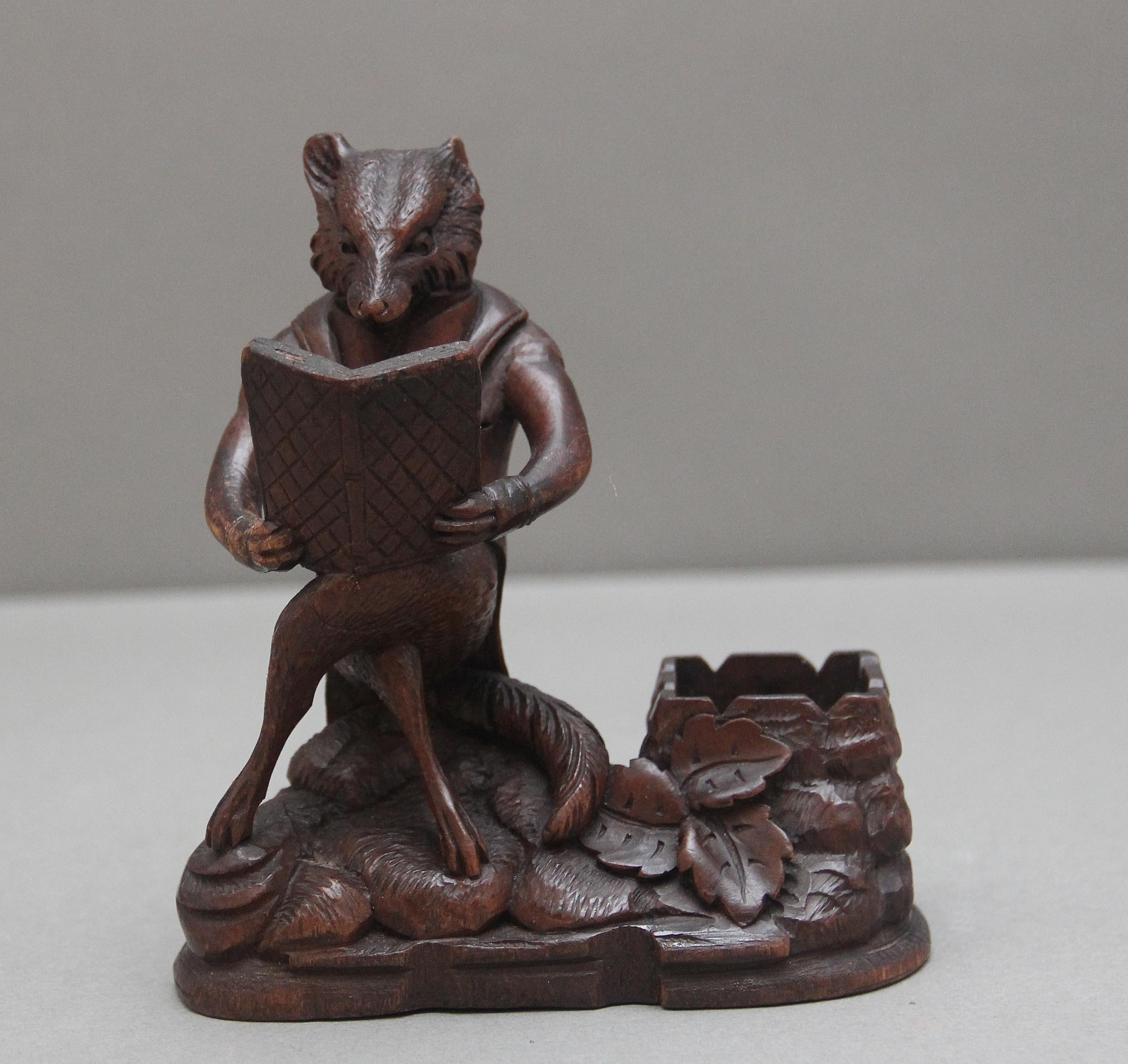 A lovely ornate 19th Century black forest carving of a fox, sitting cross legged reading a book, the fox wearing a jacket and seems to be sitting on a rock with various foliage and a carved box to the side.  Slight damage to left ear.  Circa 1880.
