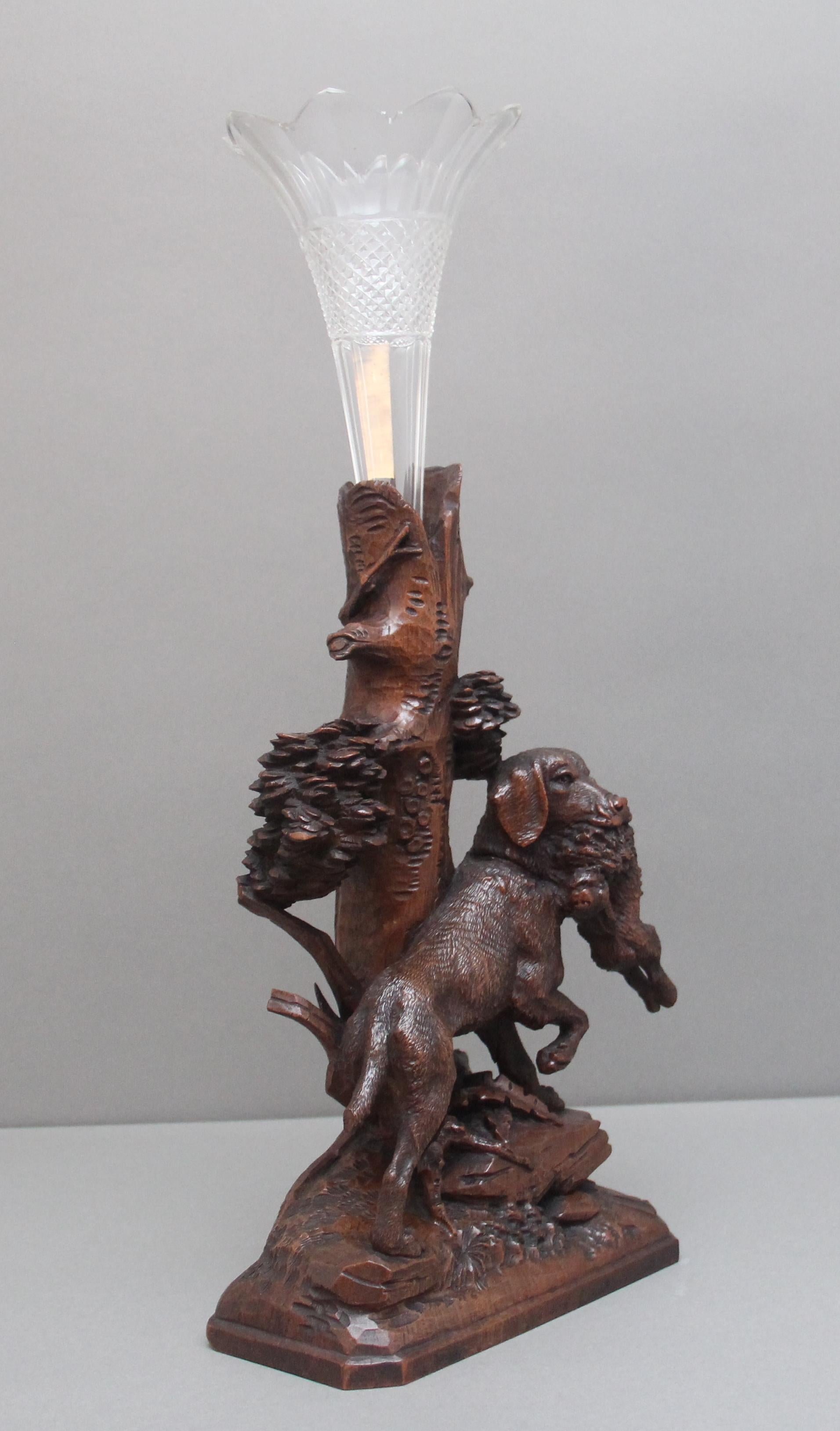 Charmante pièce centrale en forme de forêt noire du 19e siècle, avec un tronc sculpté au centre et une tige en verre amovible au bord festonné, un grand chien de chasse debout sur un sol rocailleux parmi divers feuillages avec un lièvre dans sa