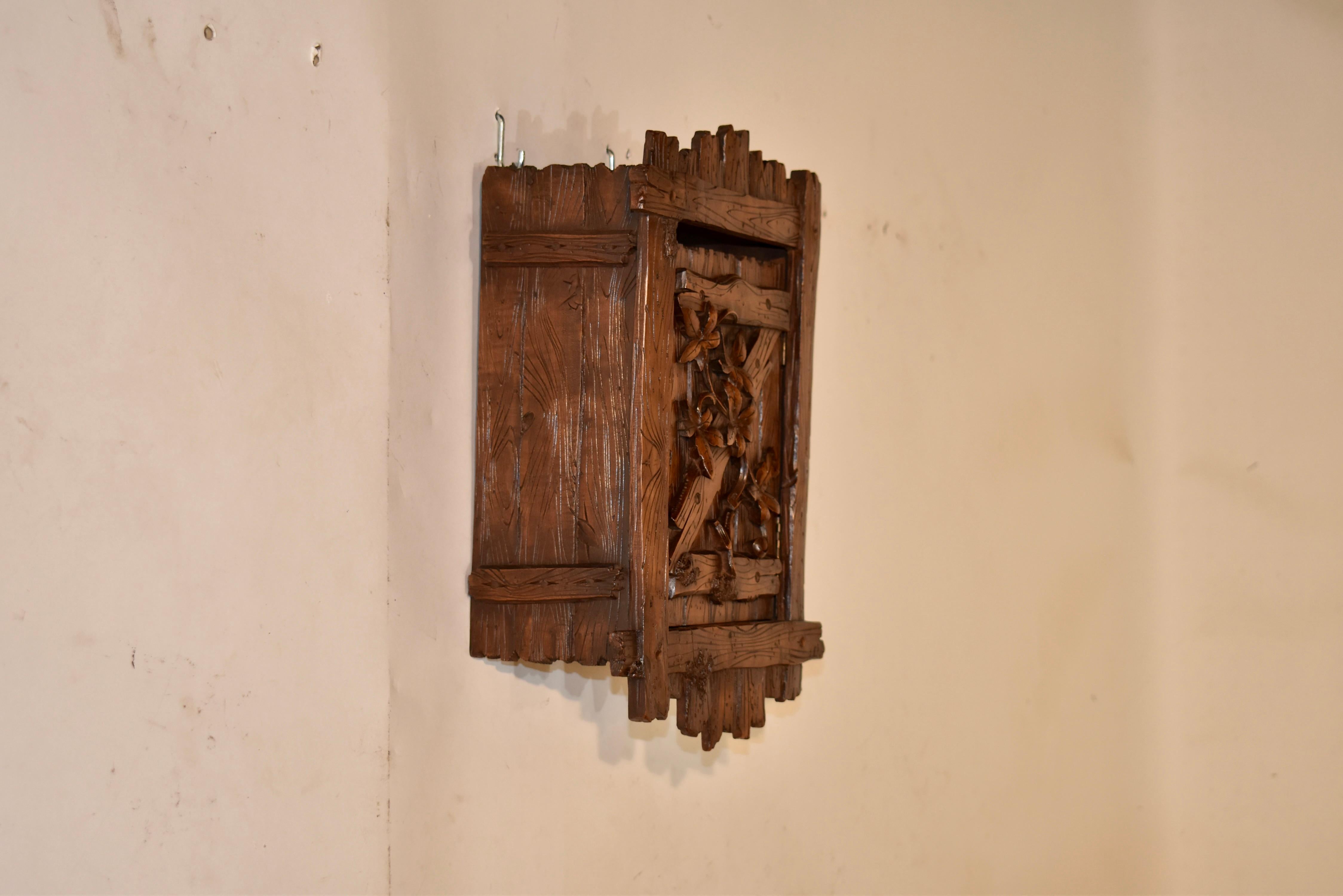 Petite boîte murale suspendue de la Forêt-Noire du 19e siècle.  L'ensemble de la pièce est sculpté à la main pour donner l'apparence de planches avec des veinures sculptées à la main.  Il y a une porte simple sur le devant, également avec