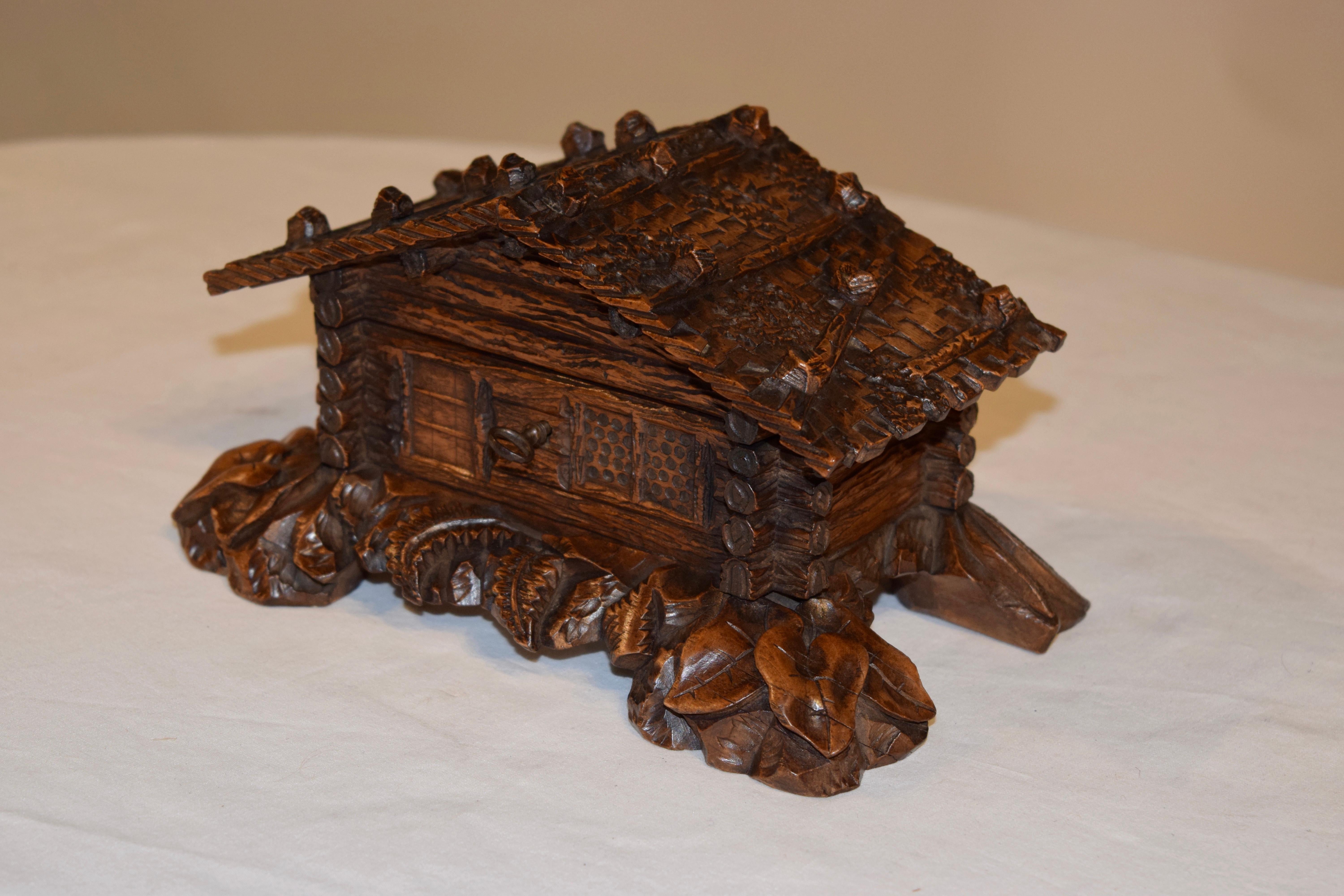 19th century black forest hand carved jewelry box from Switzerland in the shape of a cottage. The entire cottage has exquisite detail in the carving, and is depicted as a hewn log cabin with beams on the roof and massive flora surrounding the