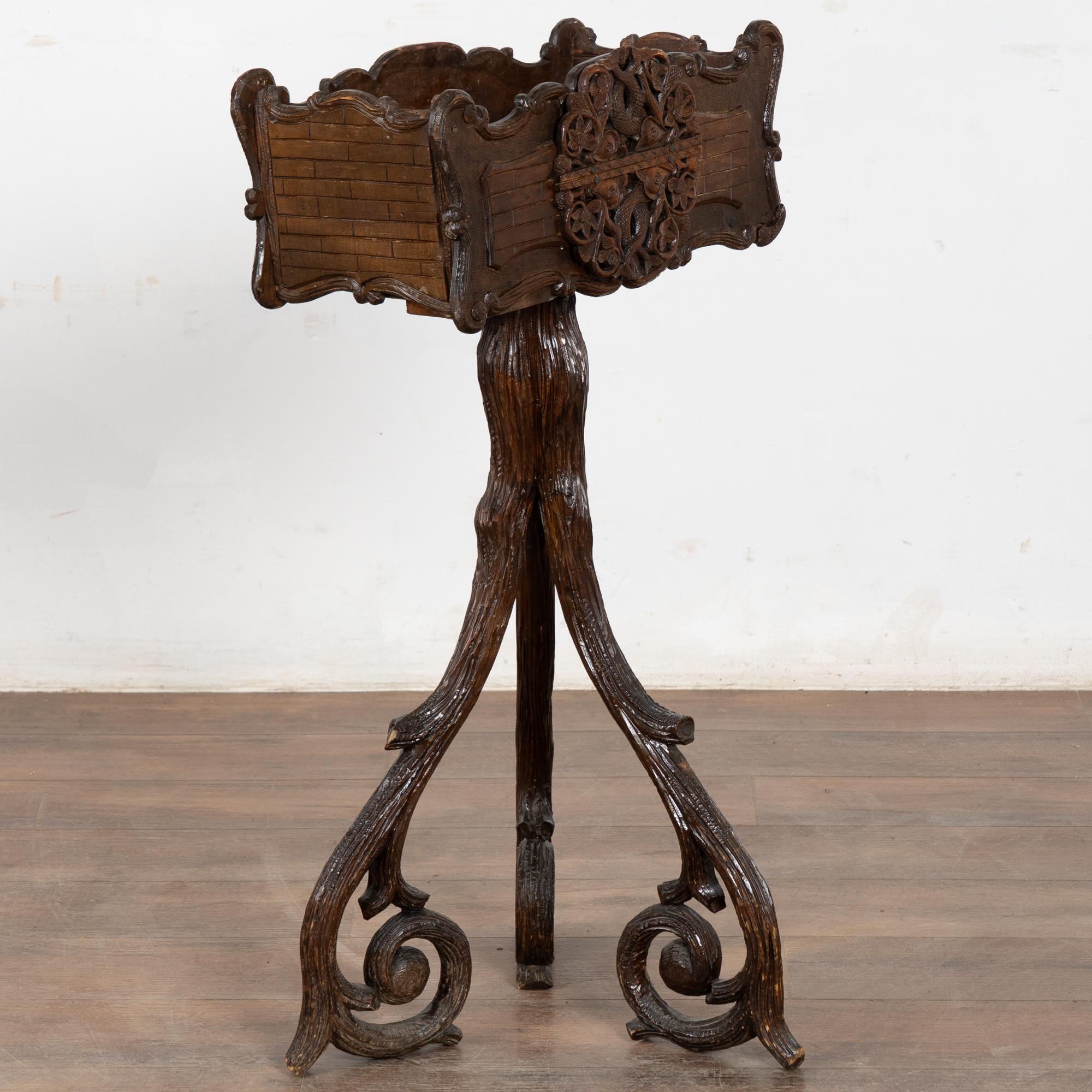 Ce porte-plante est sculpté dans le style de la Forêt-Noire, mais reflète son origine suédoise avec des queues de poisson (ou de sirène ?) entrelacées de fleurs et de vignes. La base à trois pieds est fascinante, sculptée et stylisée comme des
