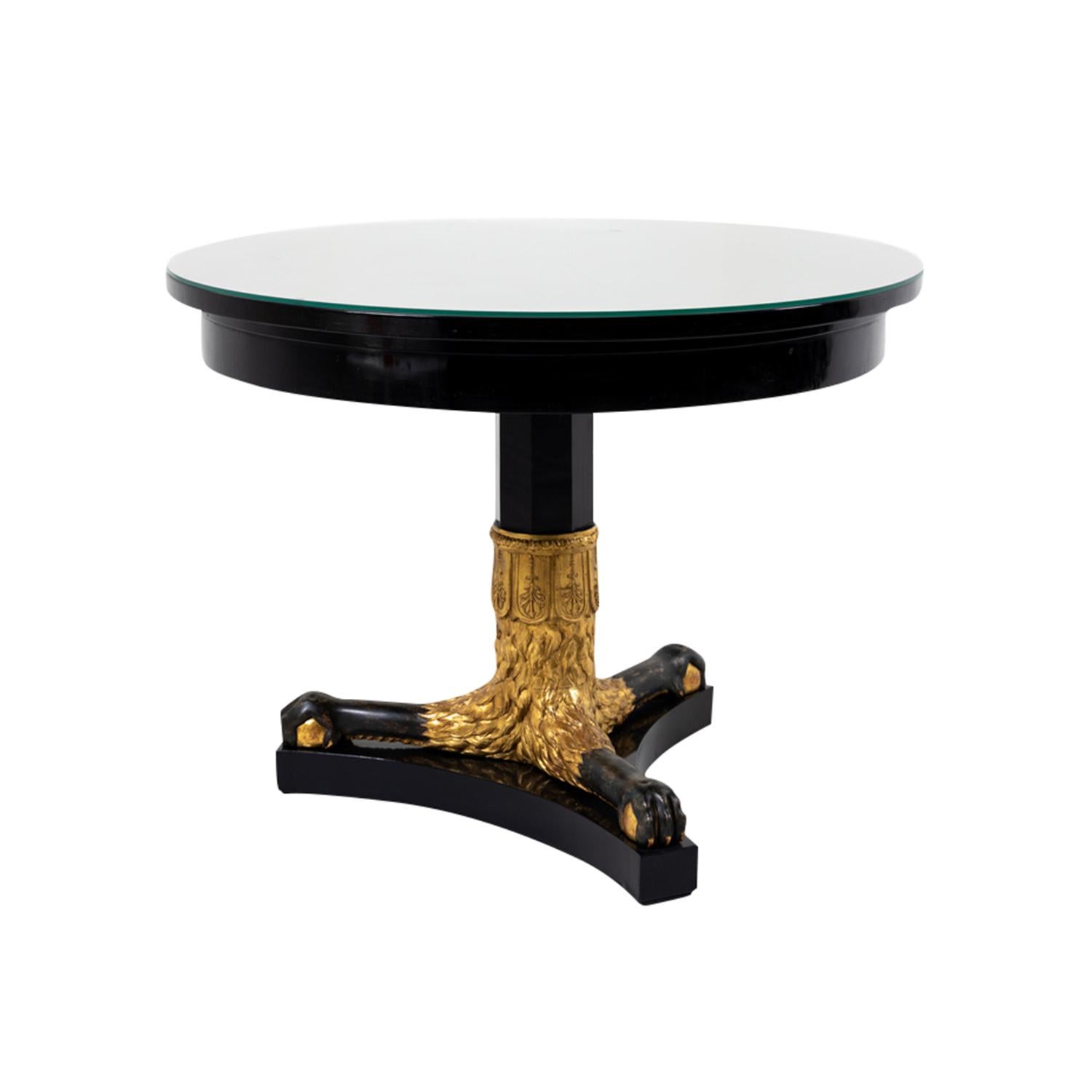 A black, antique French Empire sofa table made of hand crafted ebonized wood, in good condition. The round Parisian side table is composed with a shellac polished clear glass top to protect the surface, supported by a detailed carved gold-patinated