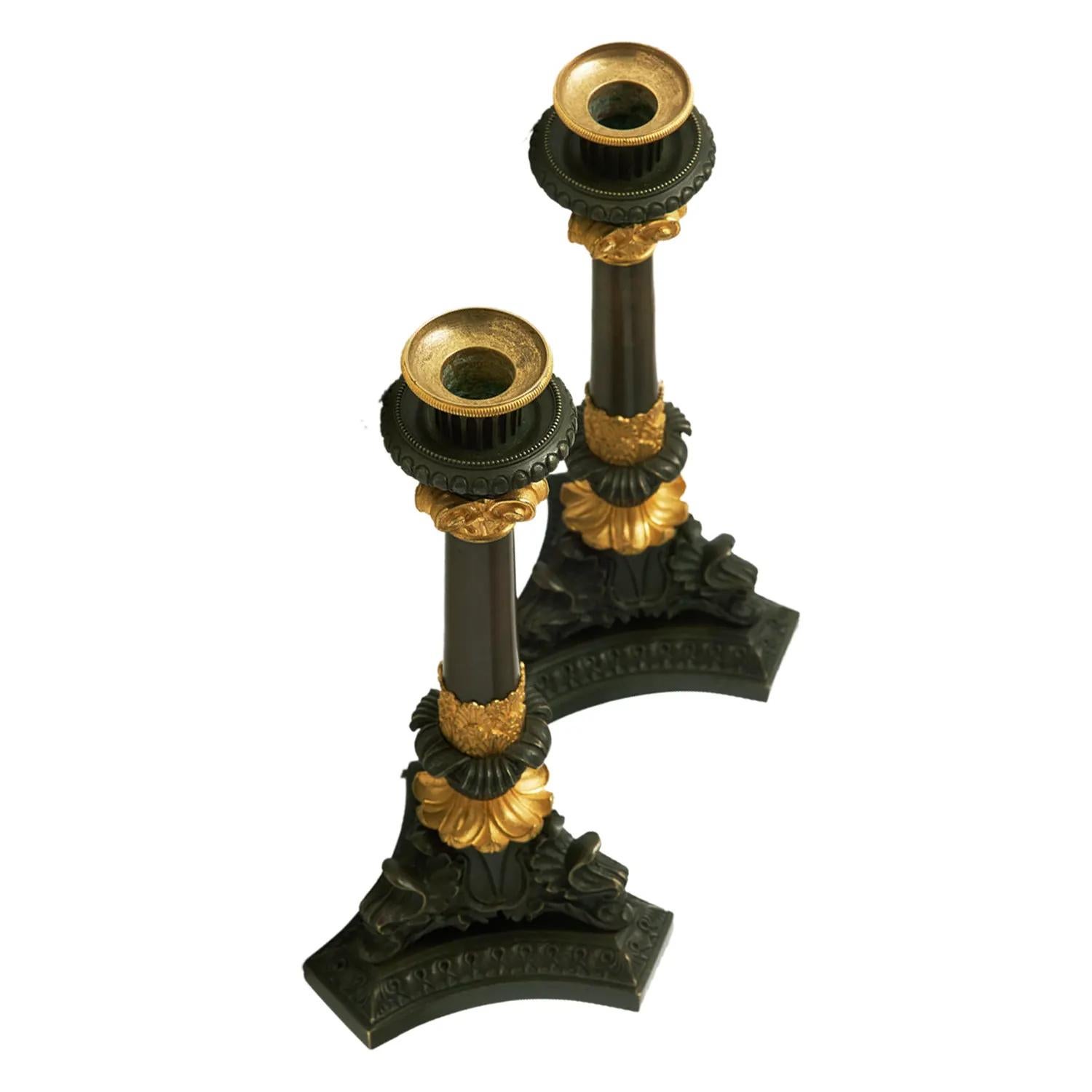 A gold-black, antique French pair of dark patinated candle sticks made of hand crafted gilded bronze, in good condition. The detailed candle holders are particularized with flowers decoration, resting on a tripod foot. The Parisian décor pieces