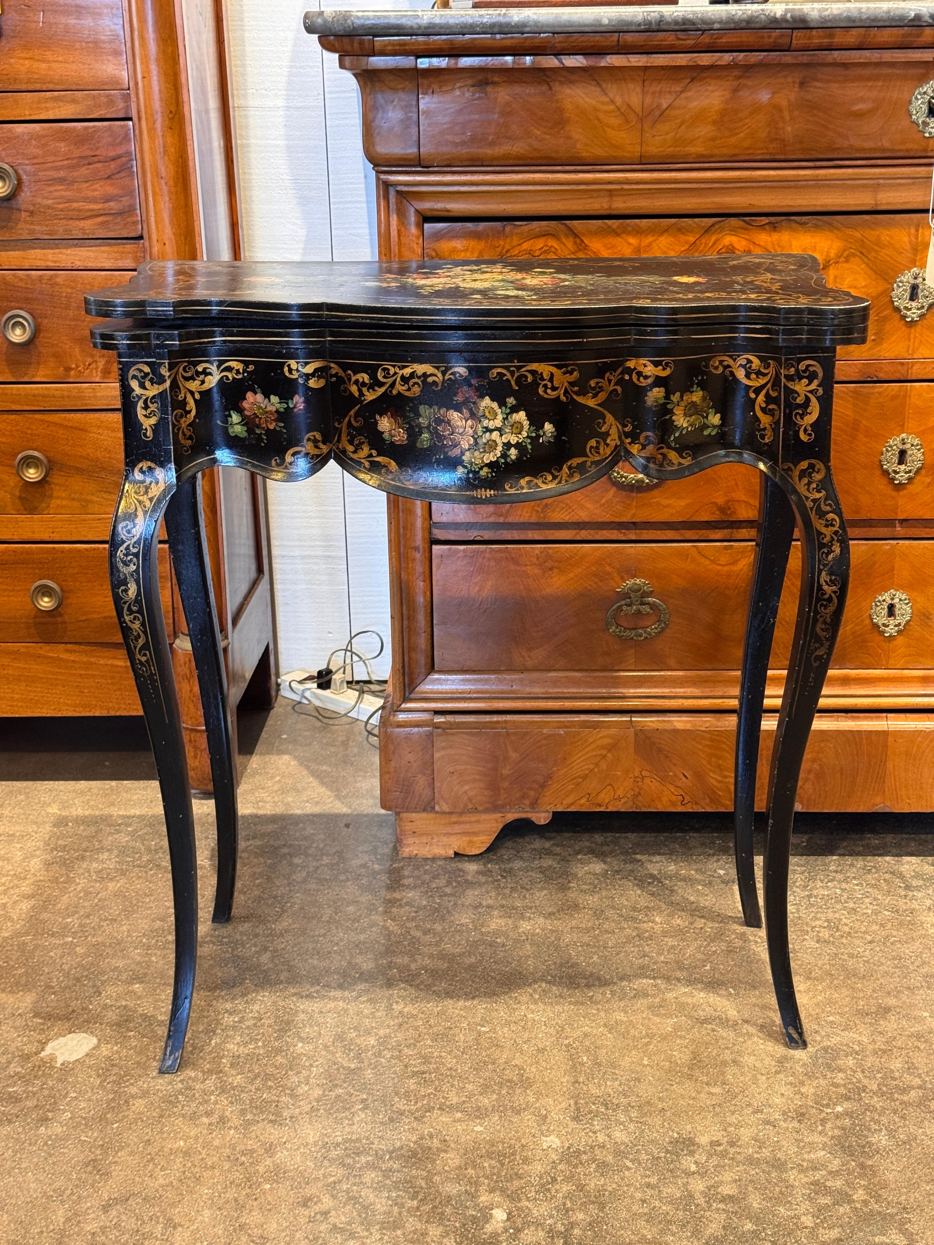 Table à jeux en laque noire du 19e siècle avec un plateau en forme, des pieds en cabriole et une décoration florale peinte à la main. Le compartiment intérieur et la surface de jeu à charnière sont montrés dans les images de détail, mettant en