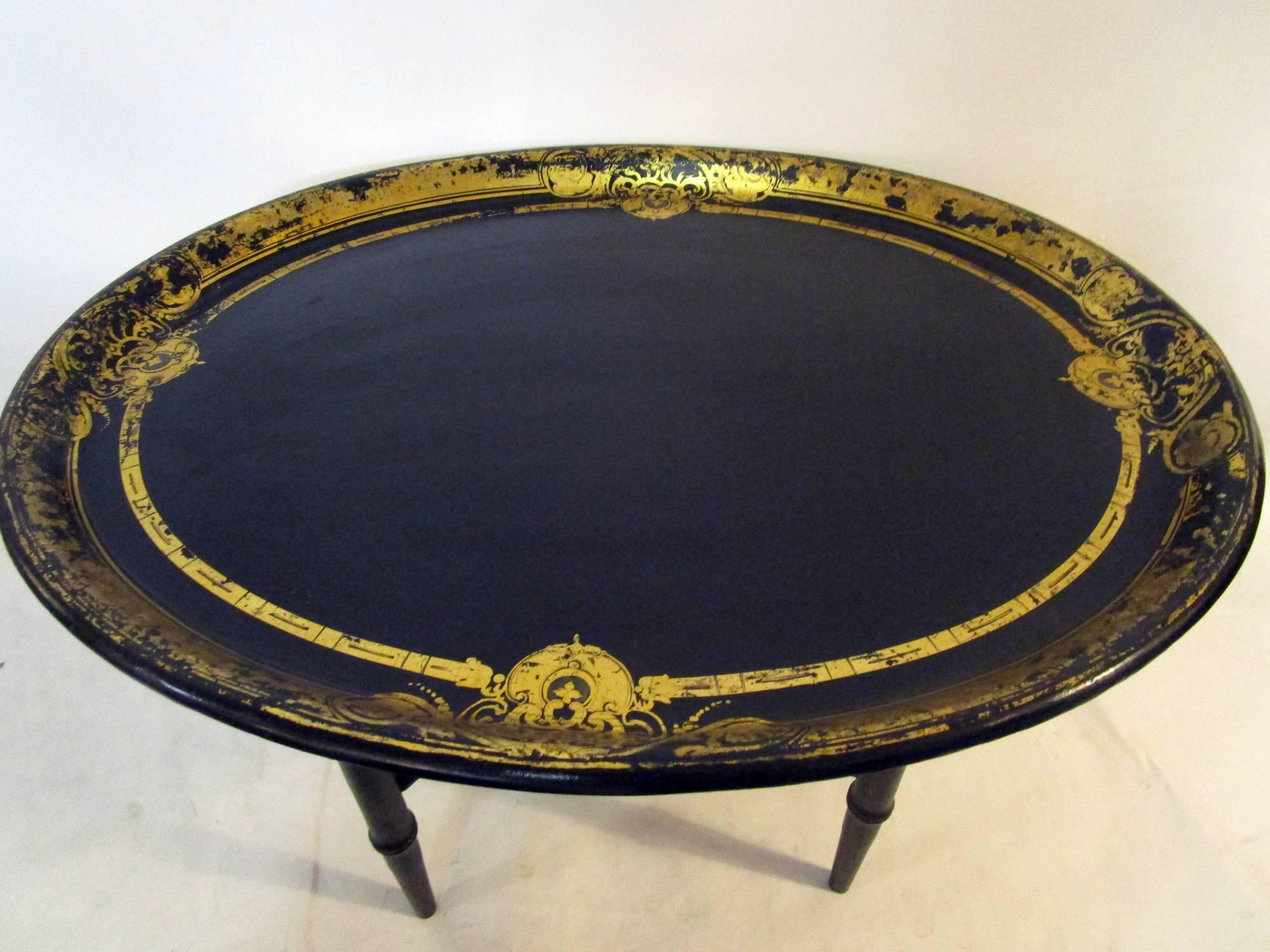 Oval shaped papier mâché tray table featuring a delicate design of gold leaf scroll work border. The sturdy adjustable wooden Chinoiserie style wooden stand is not antique but has been constructed to accommodate the English tray. The light fading to