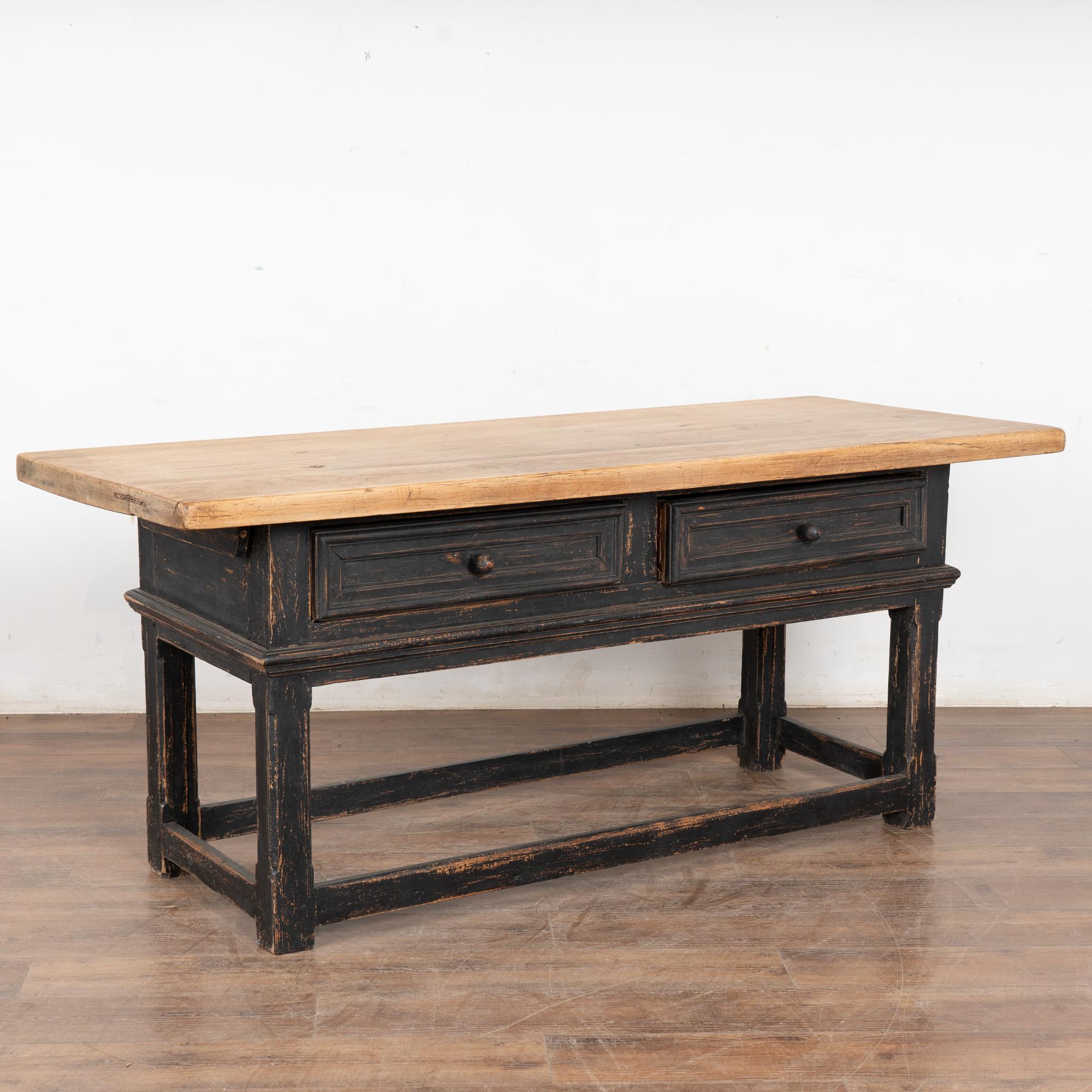 This handsome library table with two drawers rests on simple carved legs and trestle base.
The base has been given a newer, professionally applied black painted finish and is lightly distressed revealing the natural wood below while complimenting