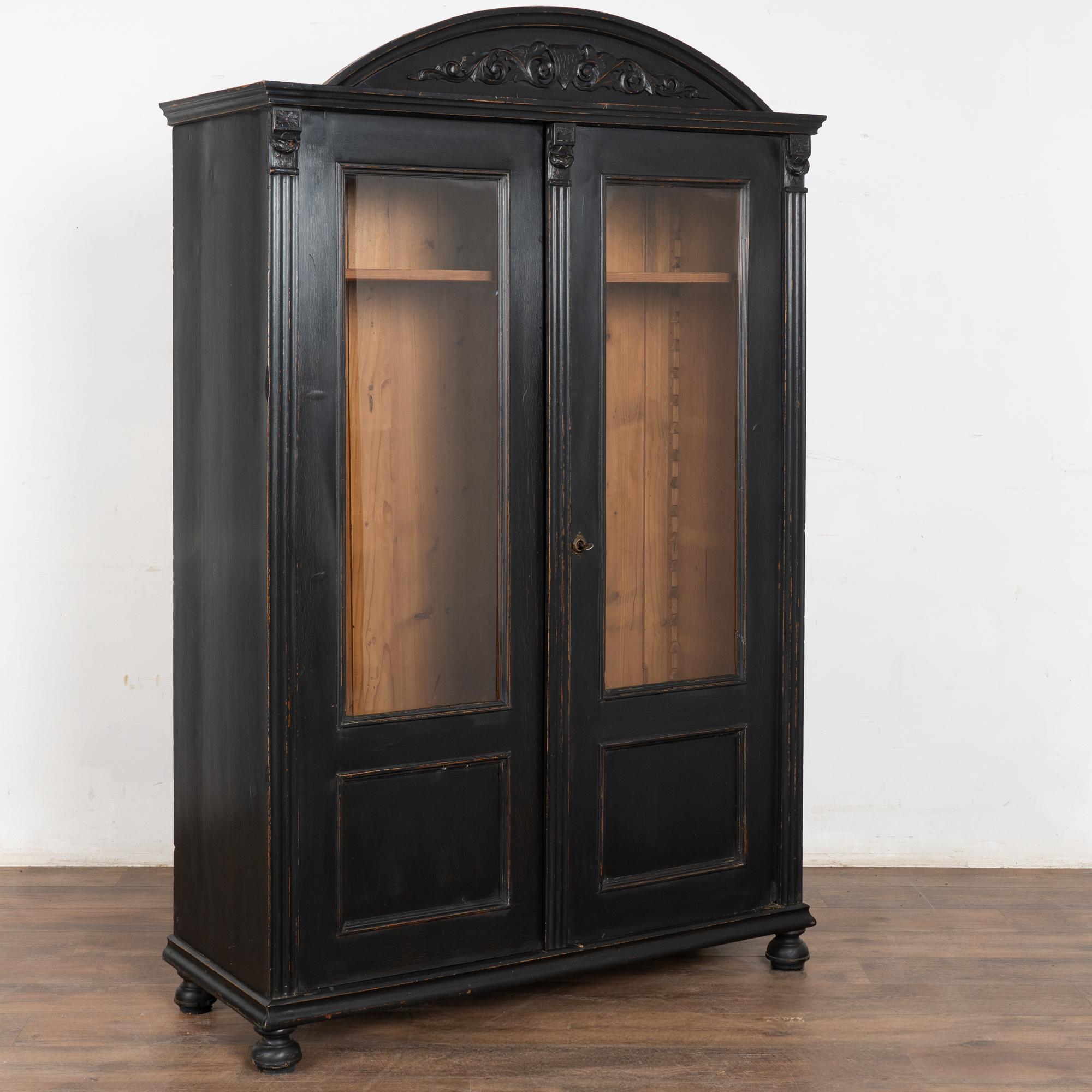 Black painted pine bookcase with carved arched bonnet or crown and two glass doors.
Restored and ready for use. Later professionally painted in black which is lightly distressed to fit the age and grace of this versatile display cabinet.
Two