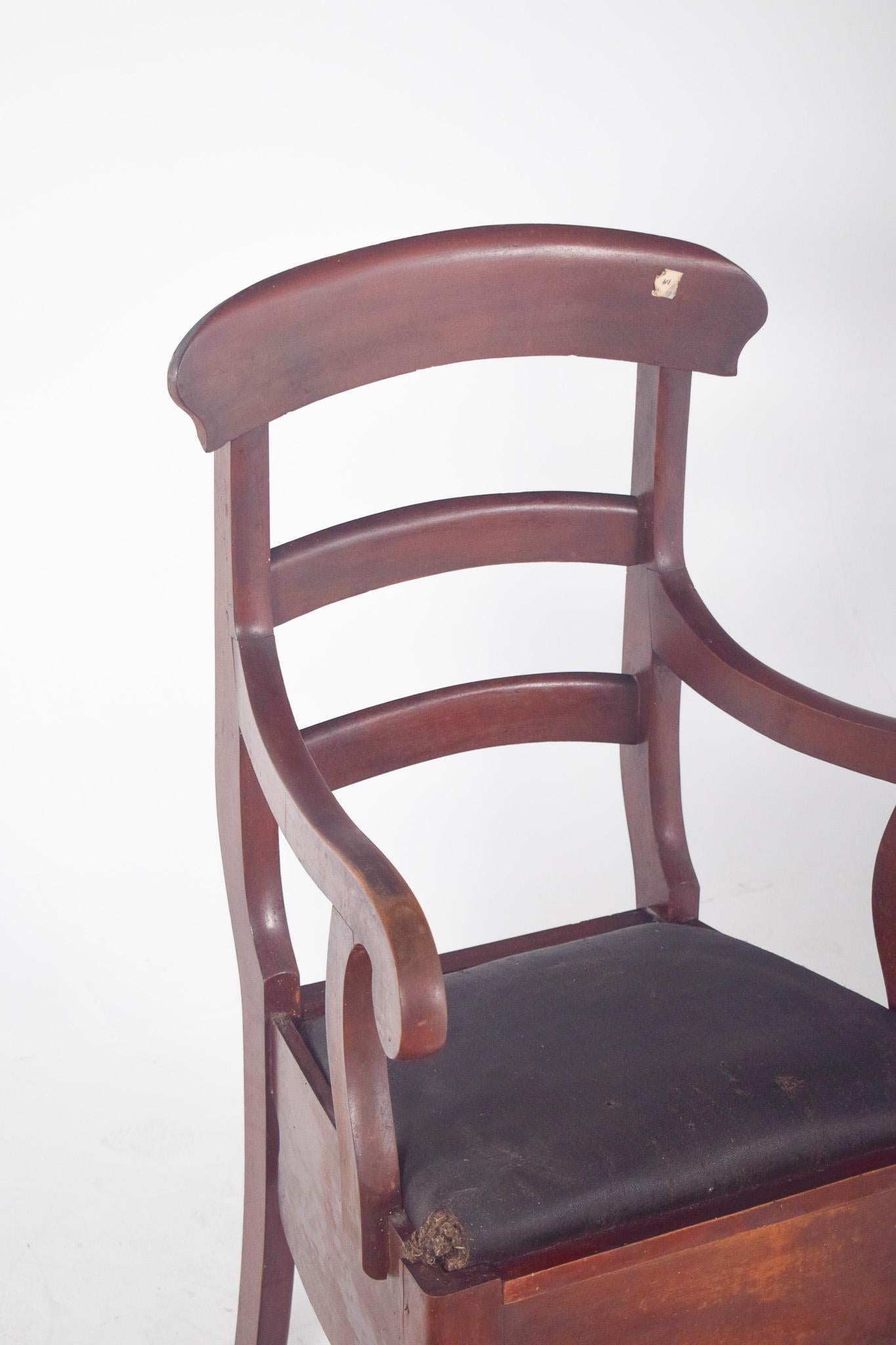 Orinal tapizado negro. Con un respaldo de tres travesaños curvados y brazos suavemente arqueados, el asiento tapizado en tela revela su uso pensando en la comodidad, y debajo se encuentra el compartimento donde originalmente estaba la vajilla,