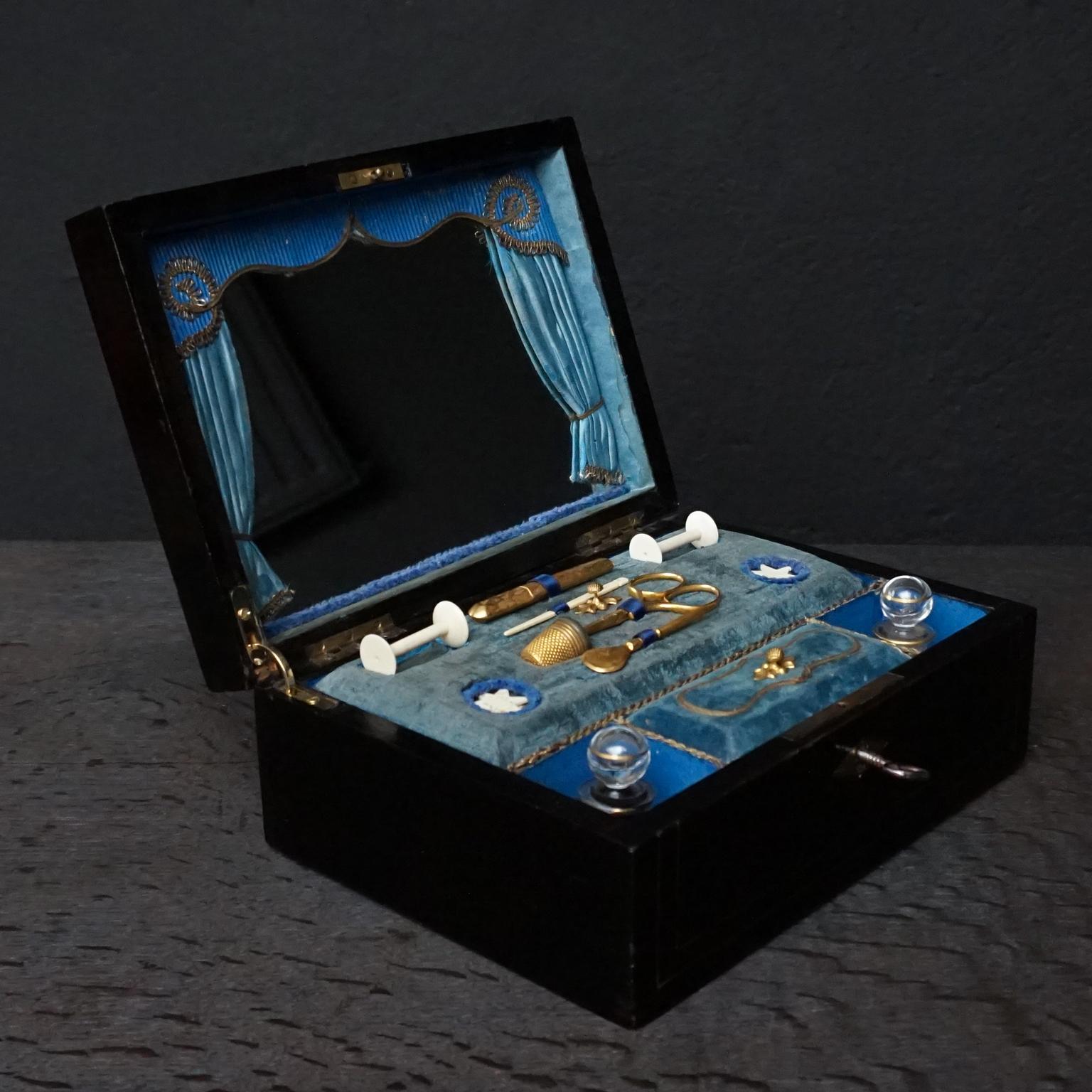 Victorian blackened wood and brass initialed vanity, sewing or writing box, the lid interior mounted with a mirror and blue silk 'curtains' like a theatre, a painted blue and blue velvet-clad tray with bone and gilt implements like bone bobbins and