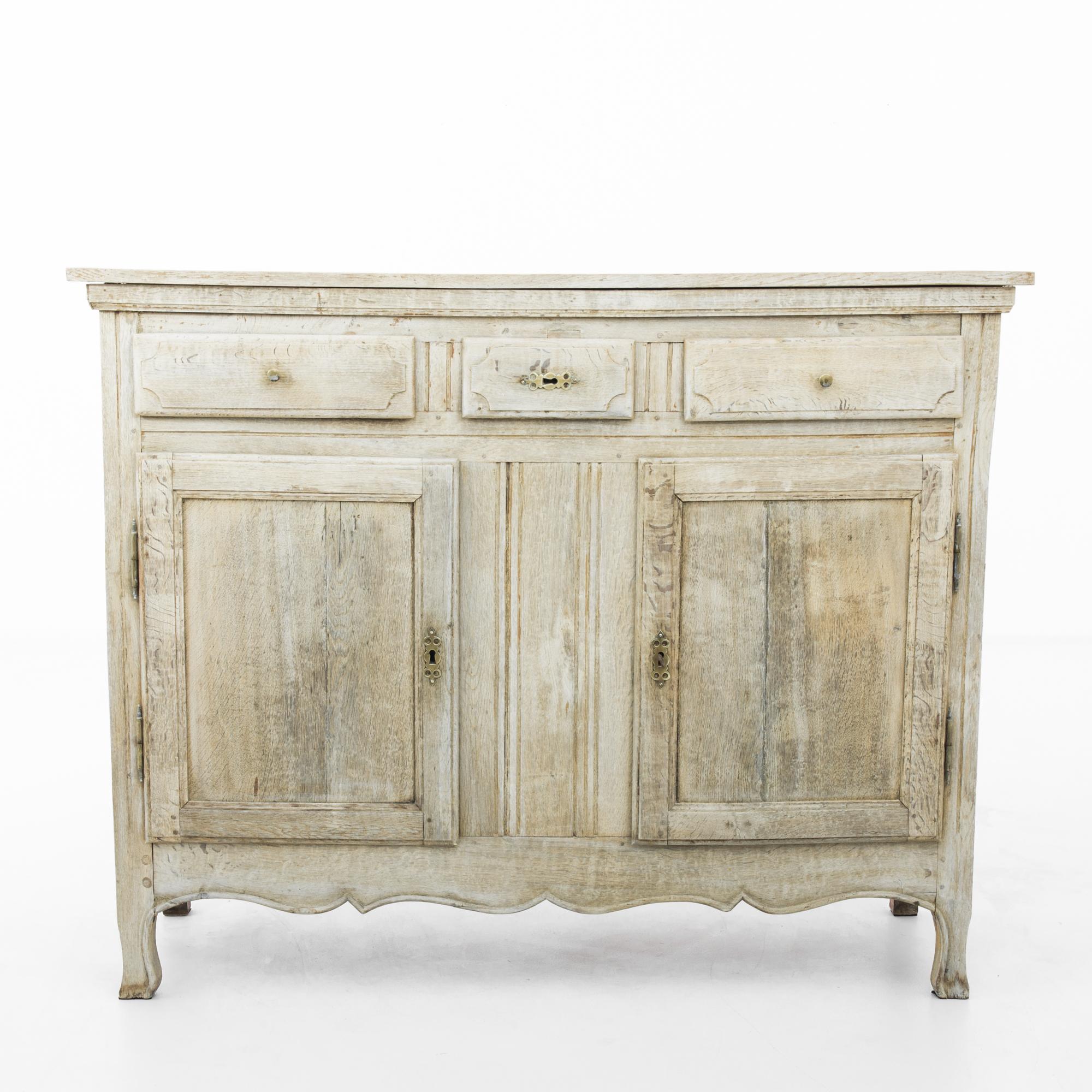 A two-door oak buffet from Belgium, circa 1850. The upright frame is subtly embellished by expressive raised panels on the cupboard doors and filigree hardware, time-worn patinated brass. Crafted in the age-old tradition of European artisans,