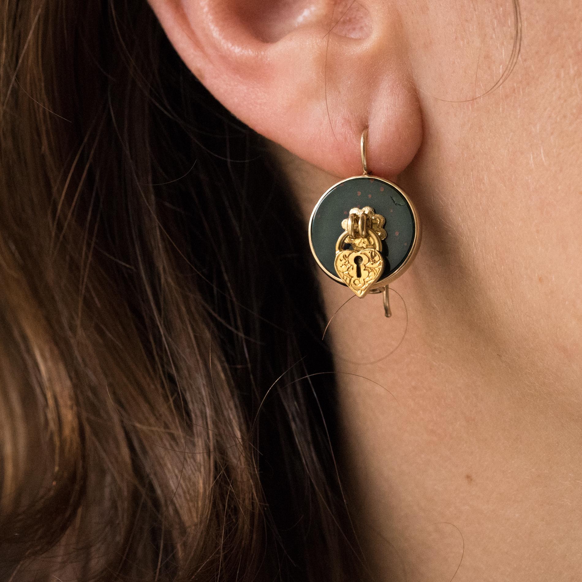 Pair of earrings in 14 karats yellow gold.
Round in shape, each is decorated with a blood jasper with a small flower in the center that holds a small padlock wich is in the shape of a chiseled heart. The hanging system is gooseneck with safety