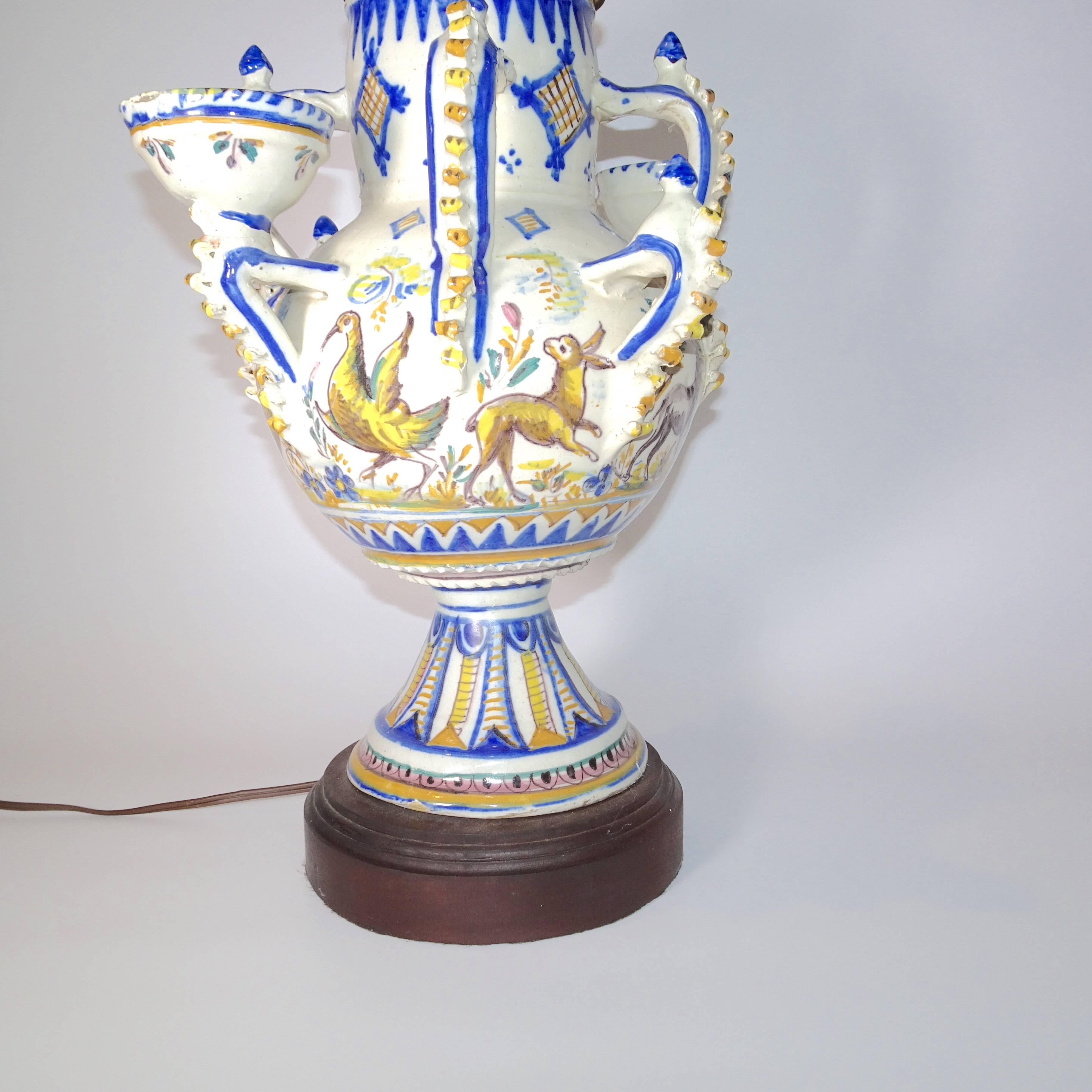 This 19th century blue and white delft table lamp with four handles and two small bowls. The pattern on the delft lamp has animals and a stylized pattern in shade of blue and gold.  A shade is available is you want to ship separately.  A nice finial