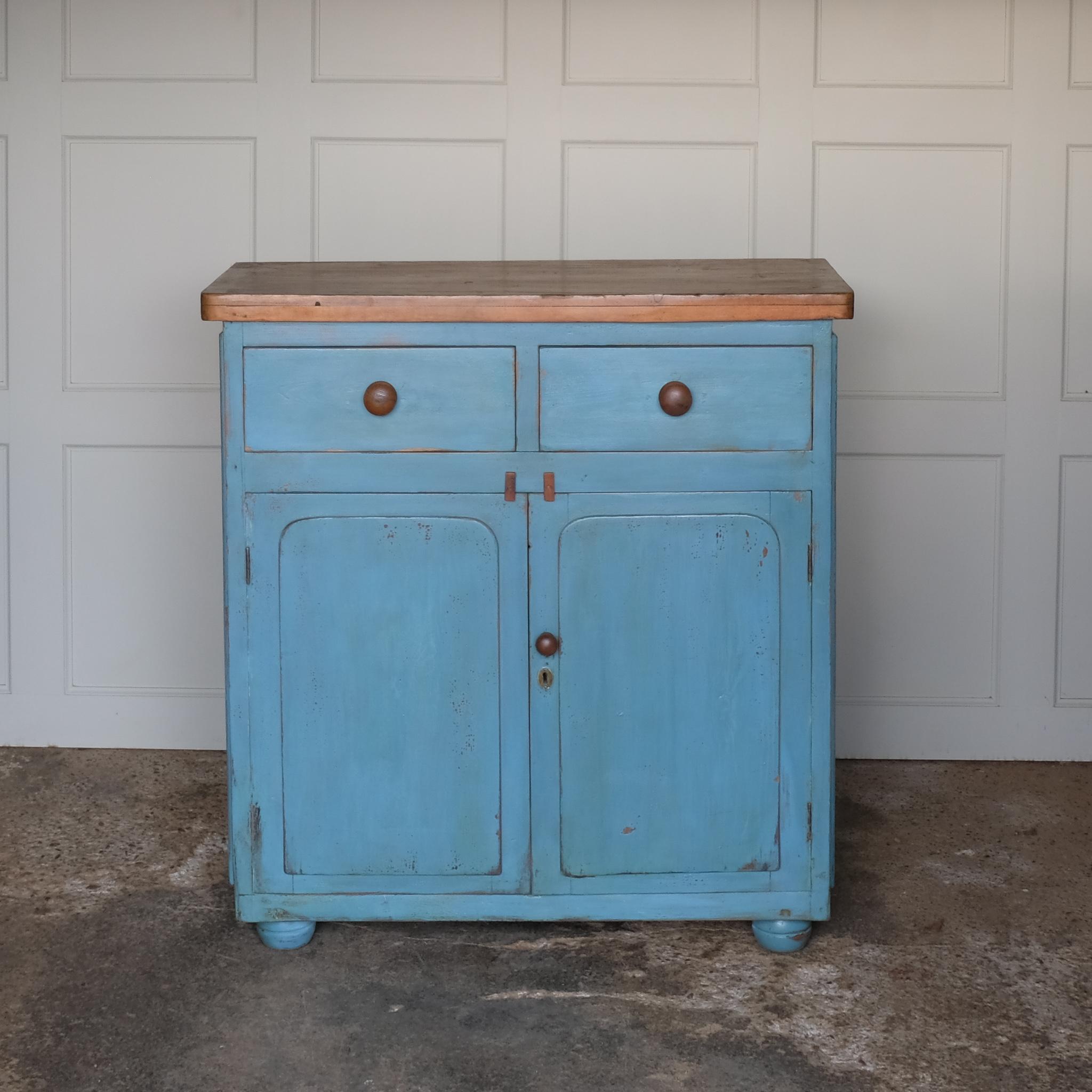 A beautiful powder blue painted cupboard, with an unpainted oak top over two drawers, above cupboard doors revealing a single shelf interior finished in a lightly contrasting yellow, on four bun feet. A lovely patina commensurate with age and use,