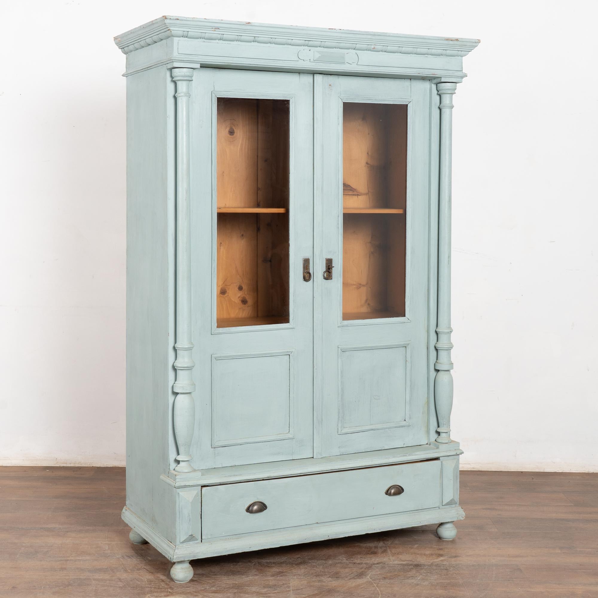 Bibliothèque en pin peint en bleu avec deux portes en verre flanquées de colonnes tournées et un seul tiroir inférieur. 
Restauré et prêt à l'emploi. Peint plus tard dans une finition bleue mate et légèrement dégradée. Notez les éraflures, les