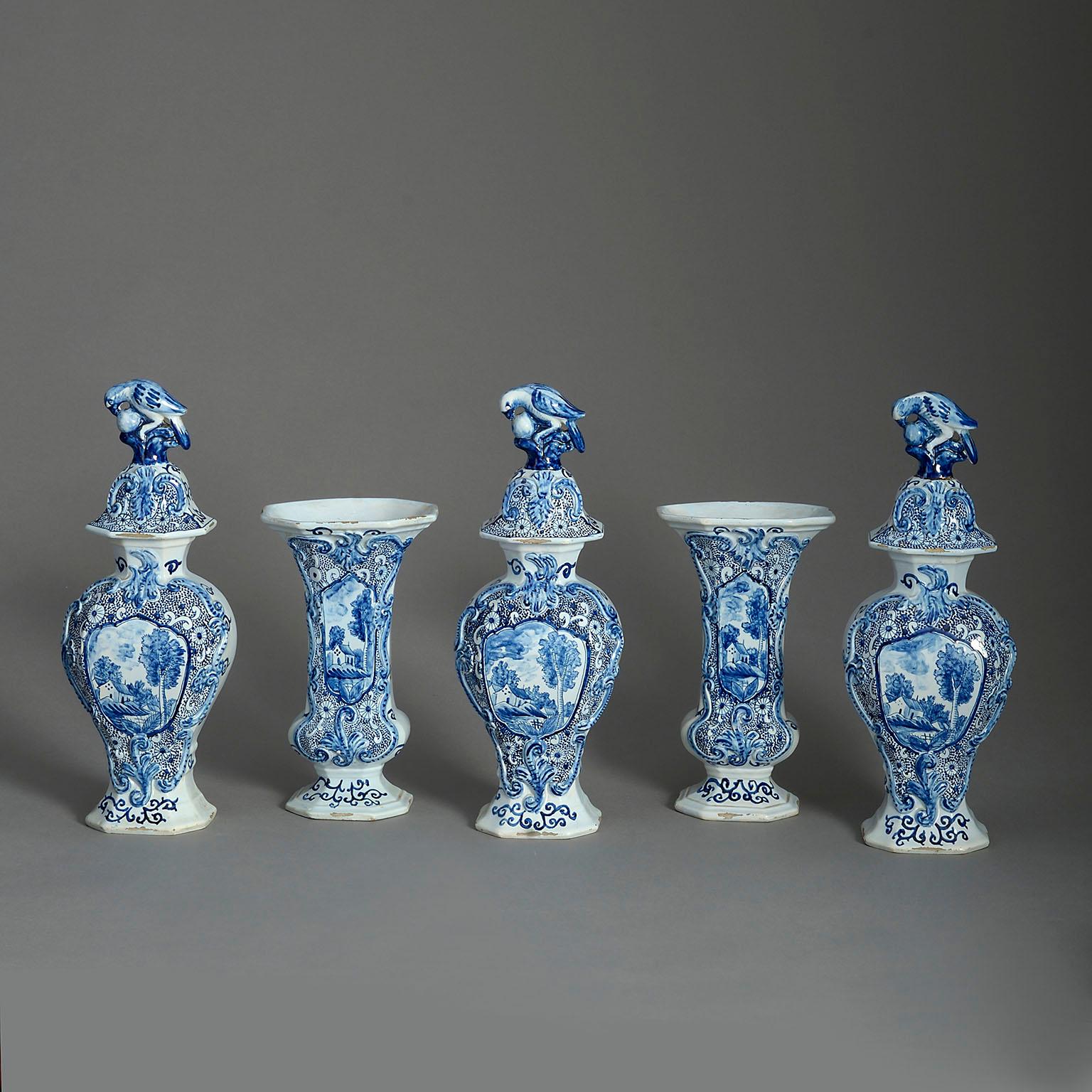 A fine late 19th century garniture of five blue and white glazed Delft pottery vases, each decorated in the Rococo manner with landscape cartouches, scrollwork, three having covers surmounted with a dove. The vases all with makers marks to the