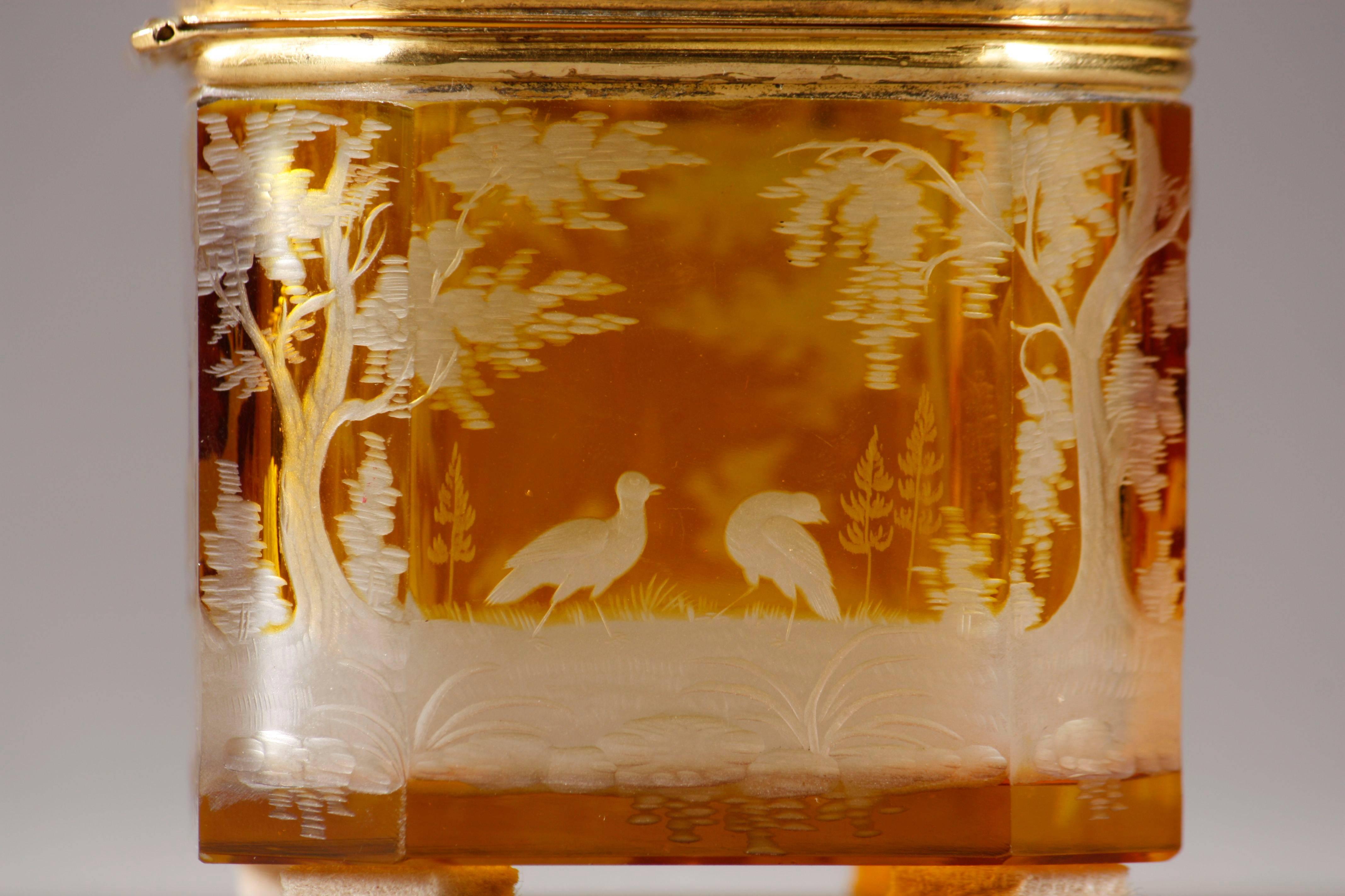 Piccolo portagioie in cristallo giallo di Boemia decorato con scene di caccia di cervi, uccelli e levrieri nella natura, tutti incisi in cristallo trasparente. La parte inferiore è decorata con un grappolo d'uva. Il soggetto e i contorni delicati
