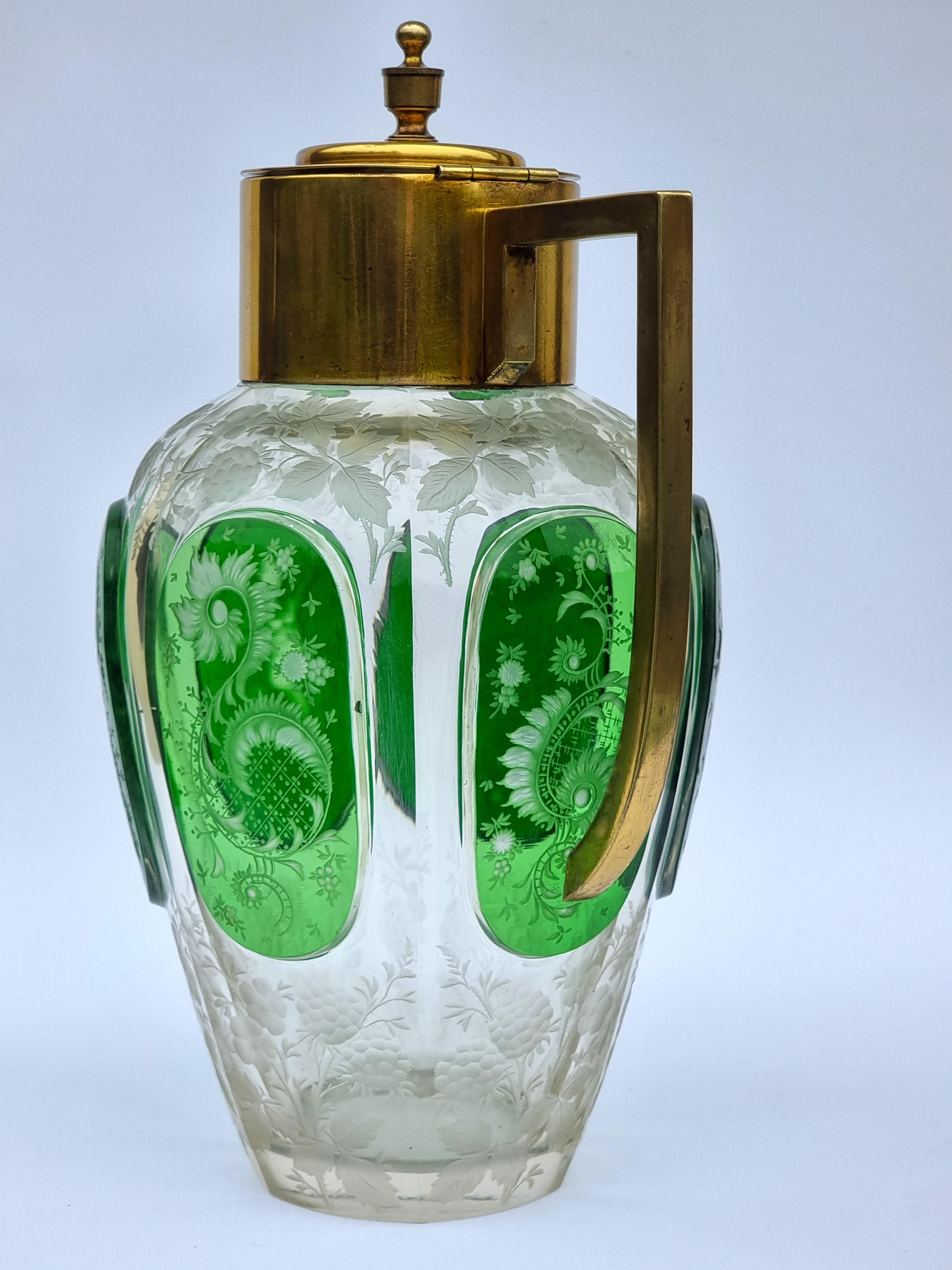 Dieser beeindruckende und schöne Rotweinkrug stammt wahrscheinlich aus böhmischer Produktion.  Sie besteht aus klarem Glas und hat in der Mitte große überlagerte grüne Glasscheiben.

Die Qualität der in das Rad eingravierten Verzierung ist sehr gut.