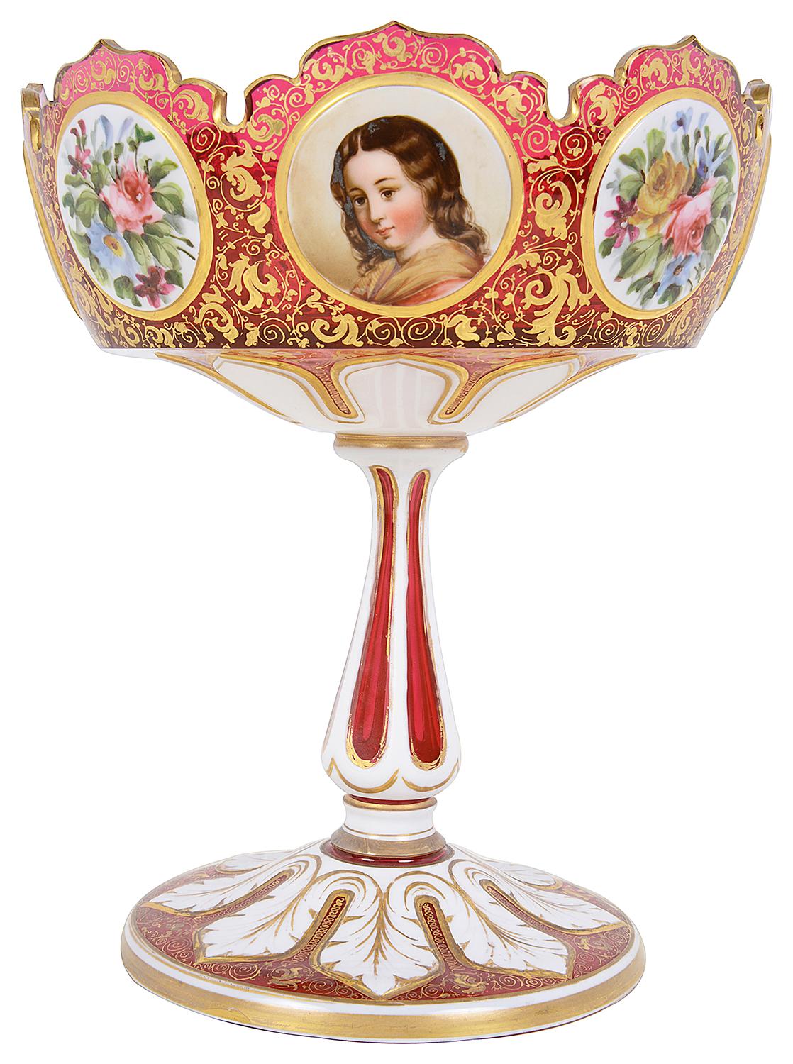 A fine quality late 19th Century Bohemian Ruby glass and white over-lay tazza, having wonderful scrolling gilded foliate decoration to the ground with inset hand painted panels depicting pretty girls and flowers, supported on an elegant fluted stem