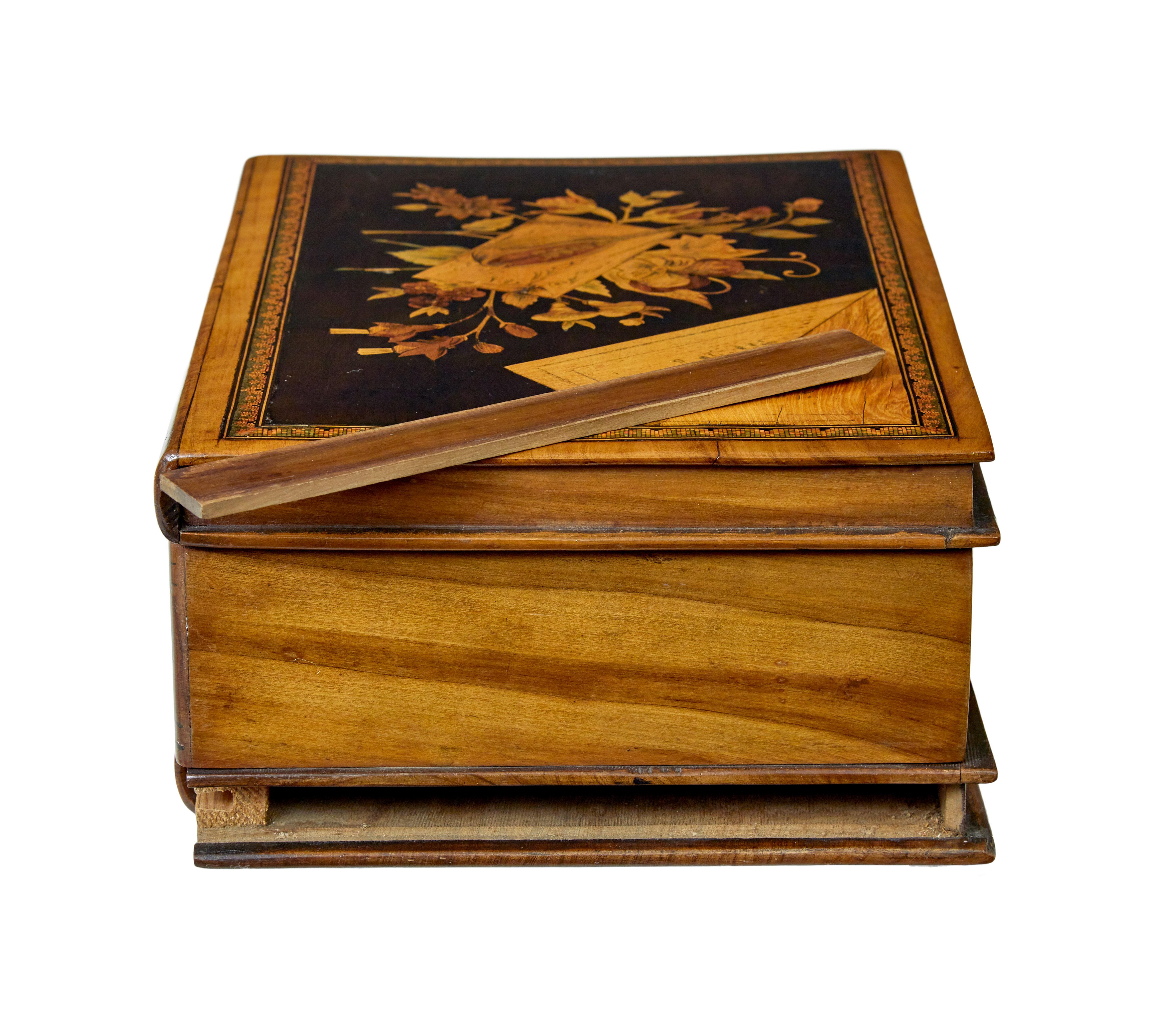 19th century book shaped inlaid olive box circa 1890.

Unusual Italian keep sake box made in olive wood.  Inlaid top surface with musical instrument, flowers and a faux peeled back corner, finished in a mosaic border.  Front of the box with hand