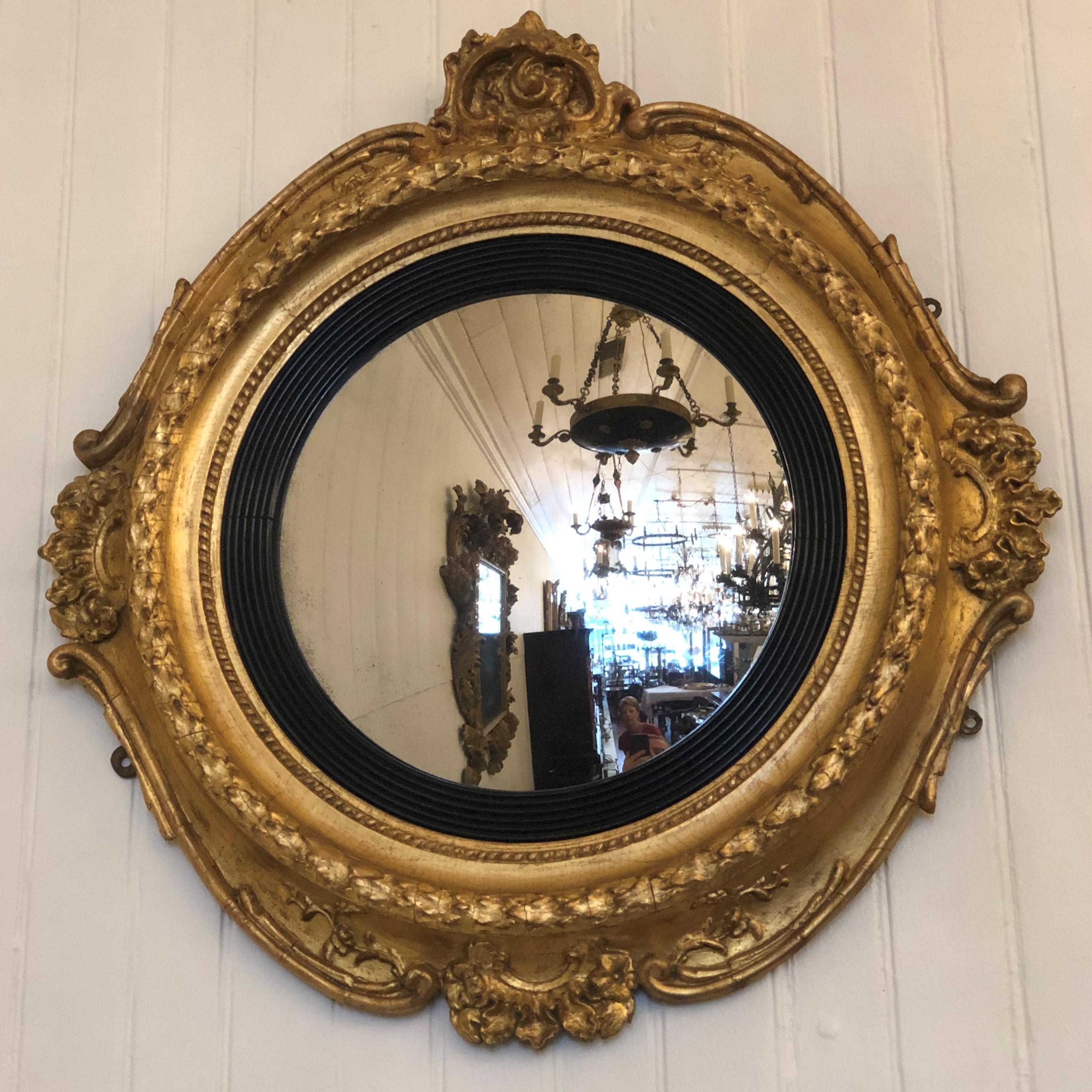 This 1830s Boston convex mirror has a wonderful scrolled frame with a foliate crest centered on the four quarters. The central feature of the frame has an oak leaf ring stepping down to a reeded ebony ring which frames the mirror.